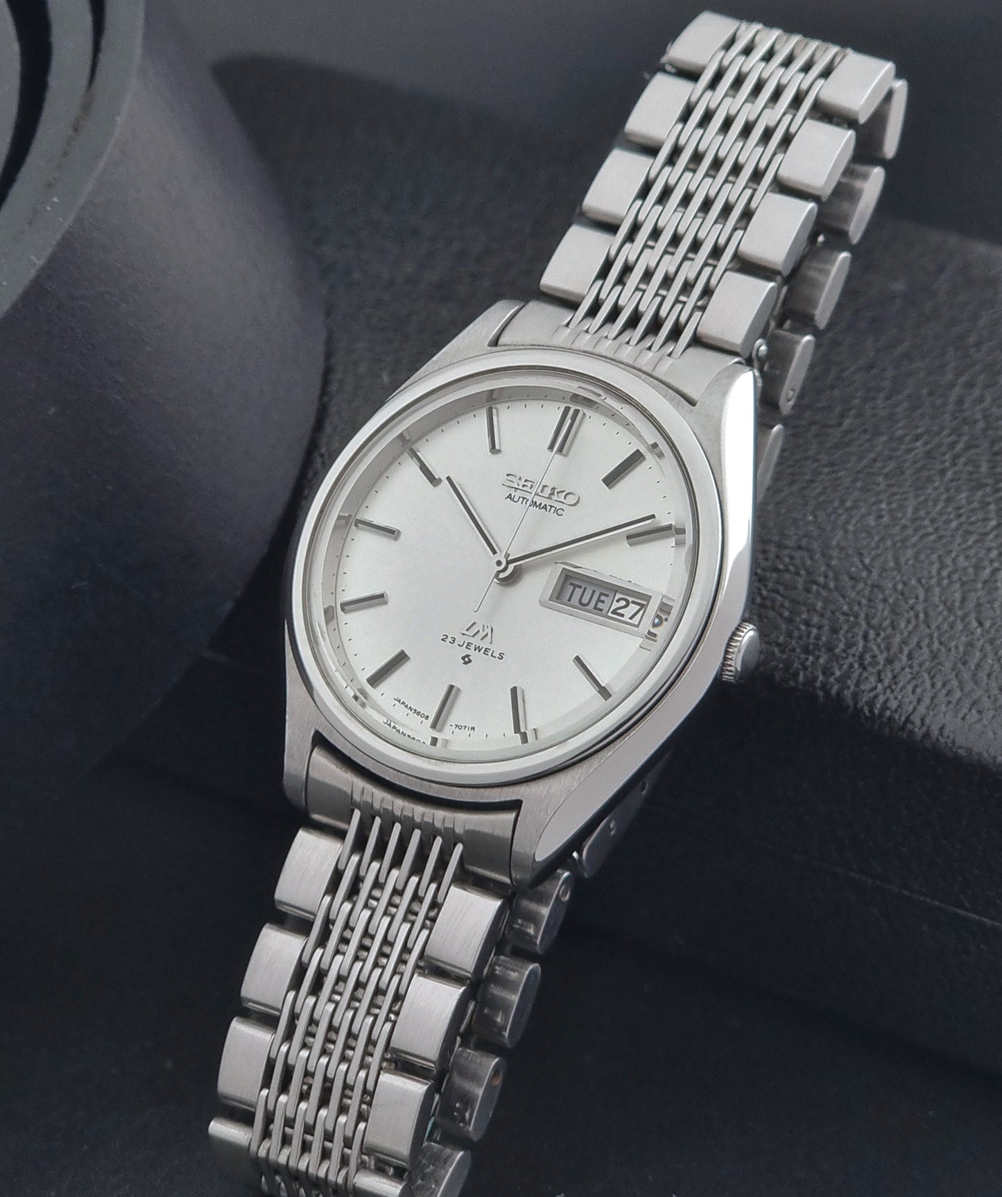 Vintage Seiko Wristwatch 5606-7071  with a metallic band on a dark background crown view