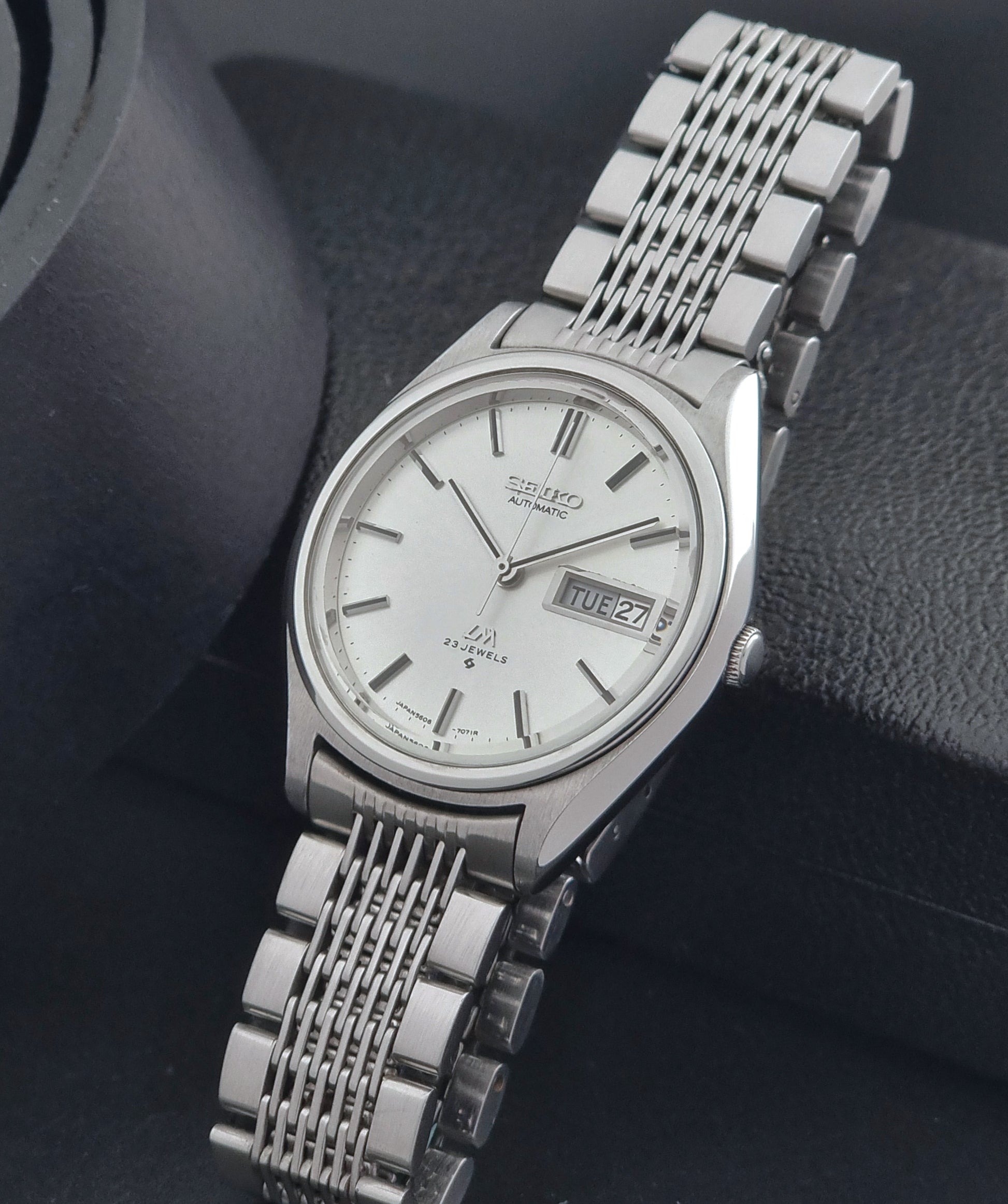 Vintage Seiko Wristwatch 5606-7071  with a metallic band on a dark background crown view