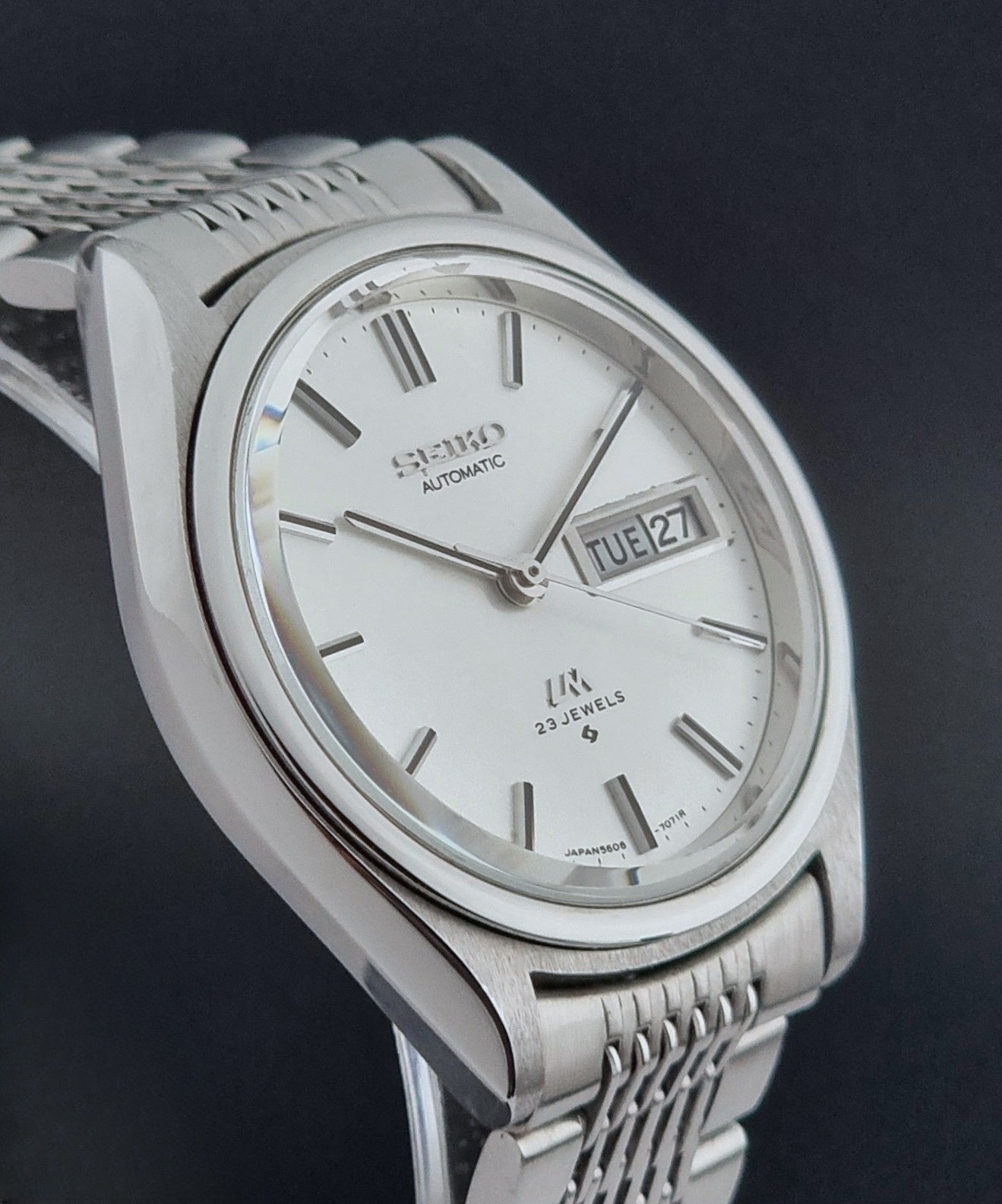 Vintage Seiko Wristwatch 5606-7071  with a metallic band on a dark background side profile view