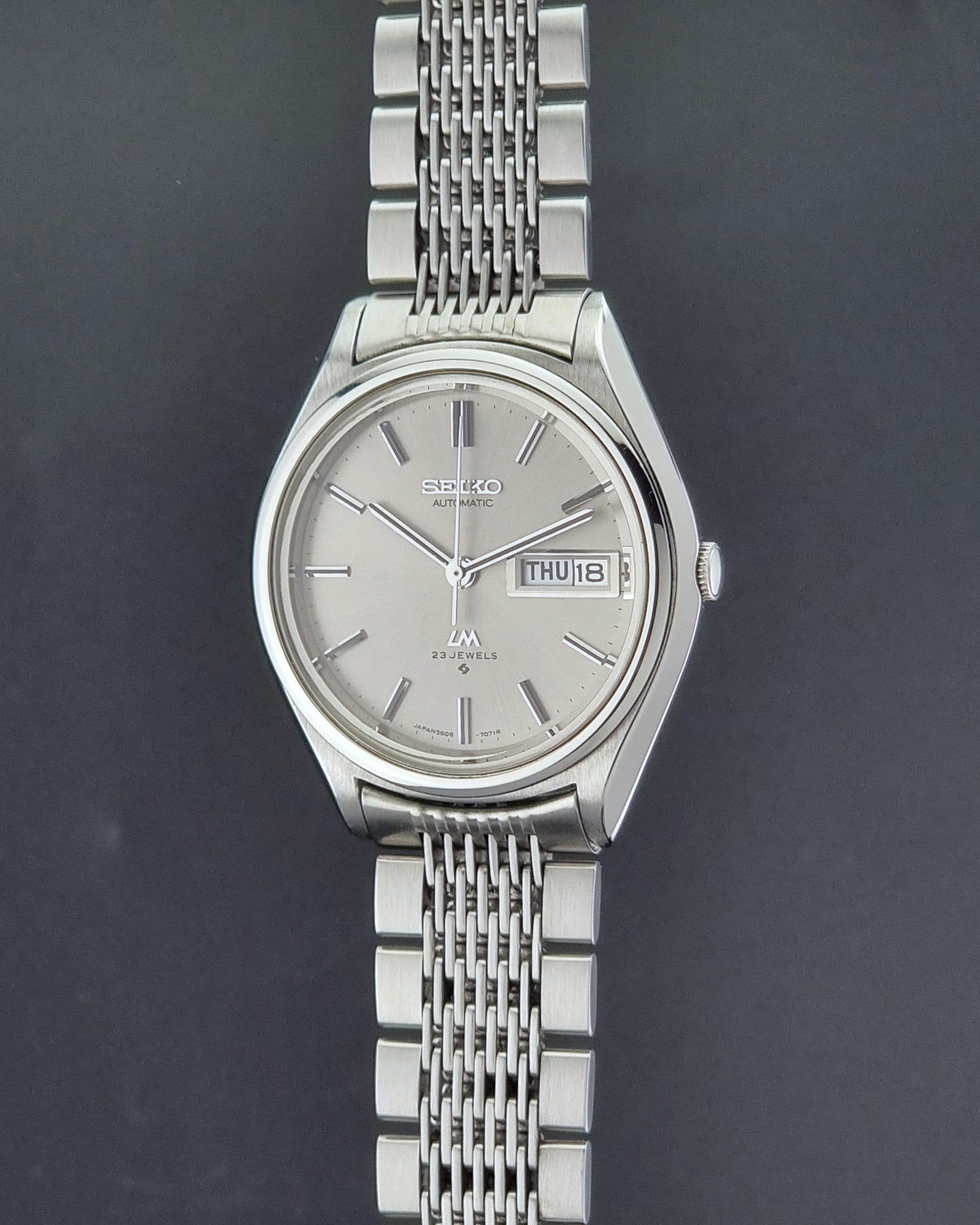 Vintage Seiko 5606-7071 LordMatic wristwatch with a metallic band on a dark gray background crown profile view