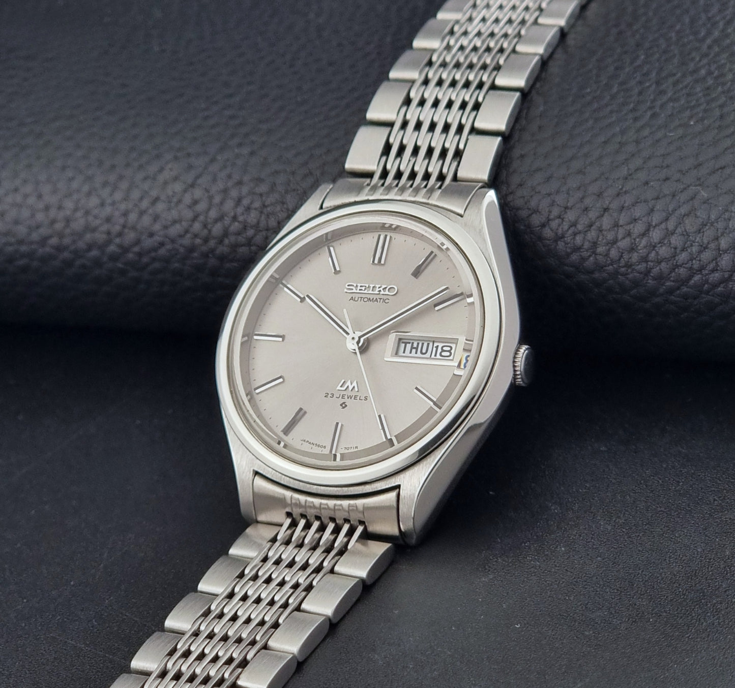Vintage Seiko 5606-7071 LordMatic wristwatch with a metallic band on a dark gray background crown view