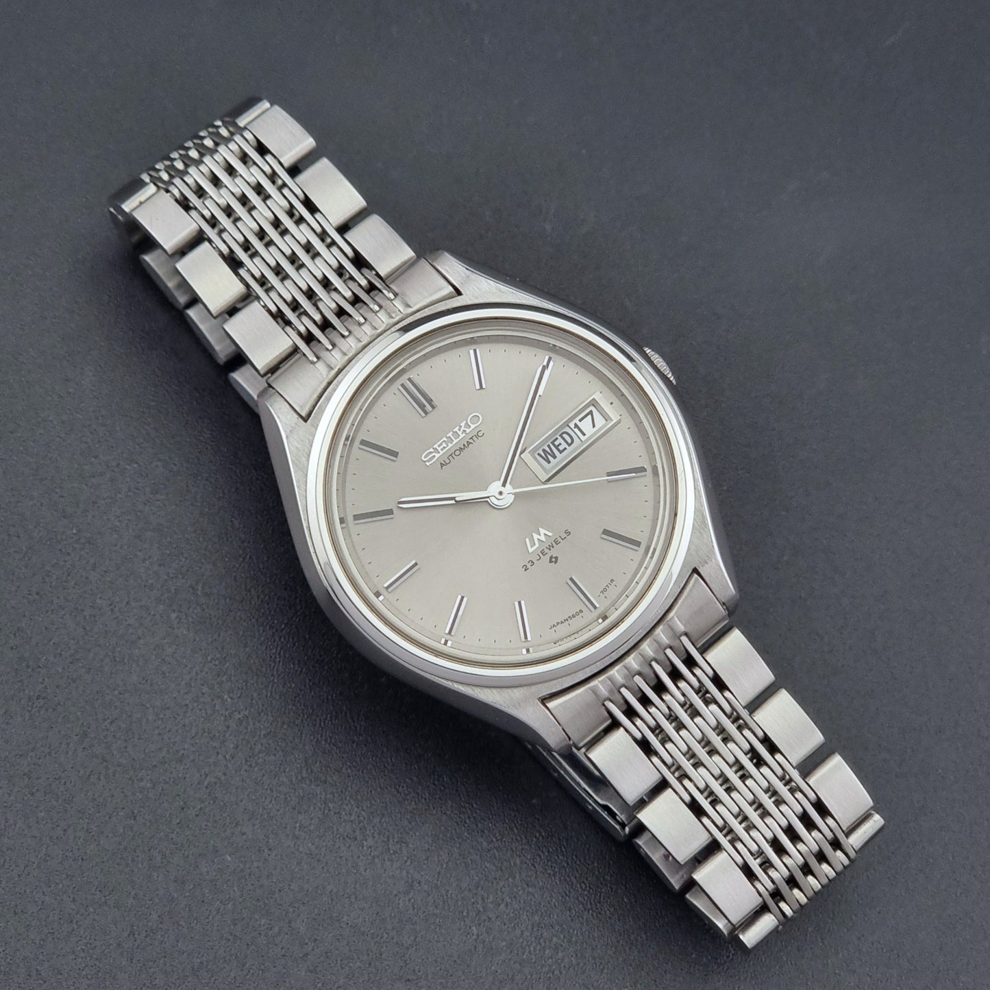 Vintage Seiko 5606-7071 LordMatic wristwatch with a metallic band on a dark gray background close dial view