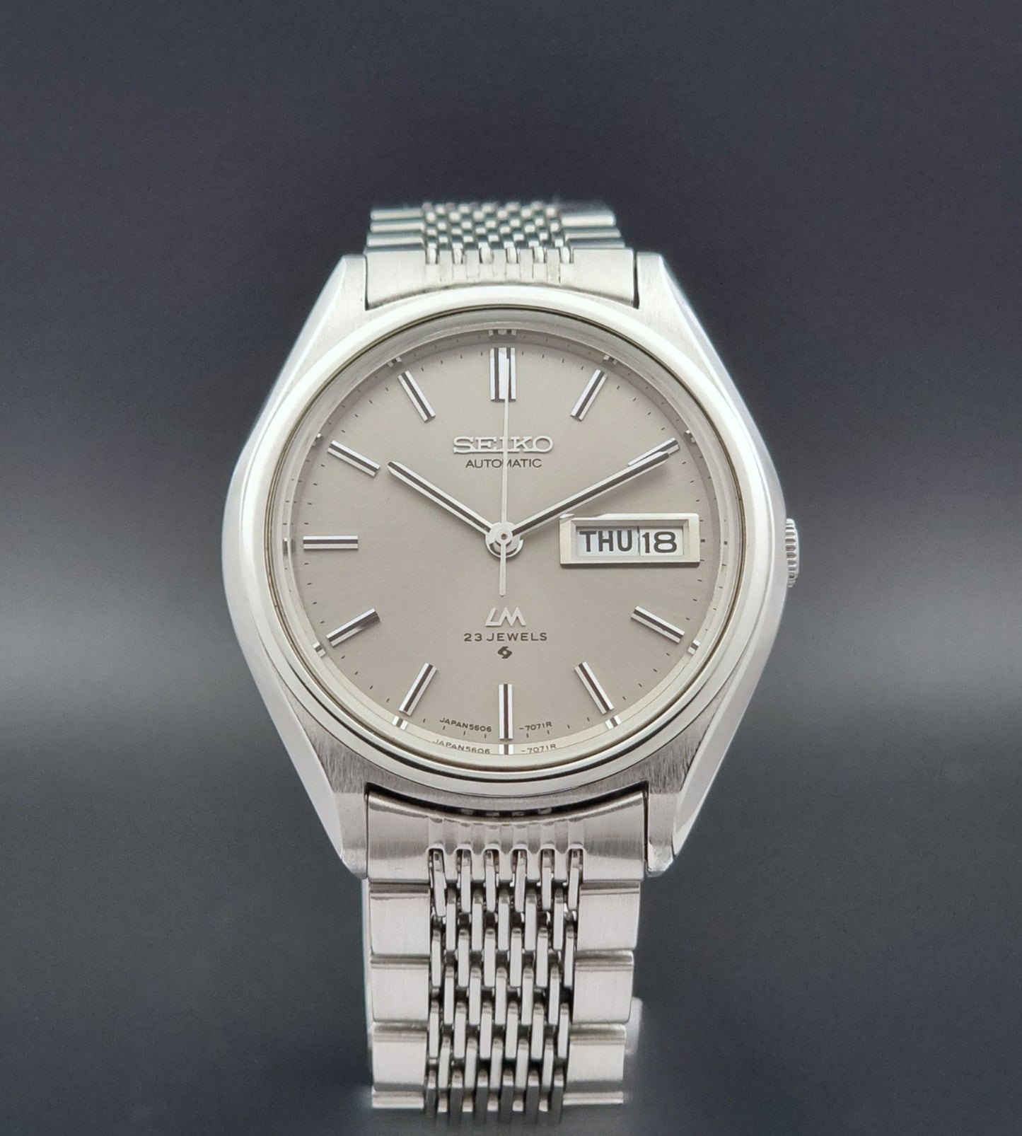 Vintage Seiko 5606-7071 LordMatic wristwatch with a metallic band on a dark gray background close dial view