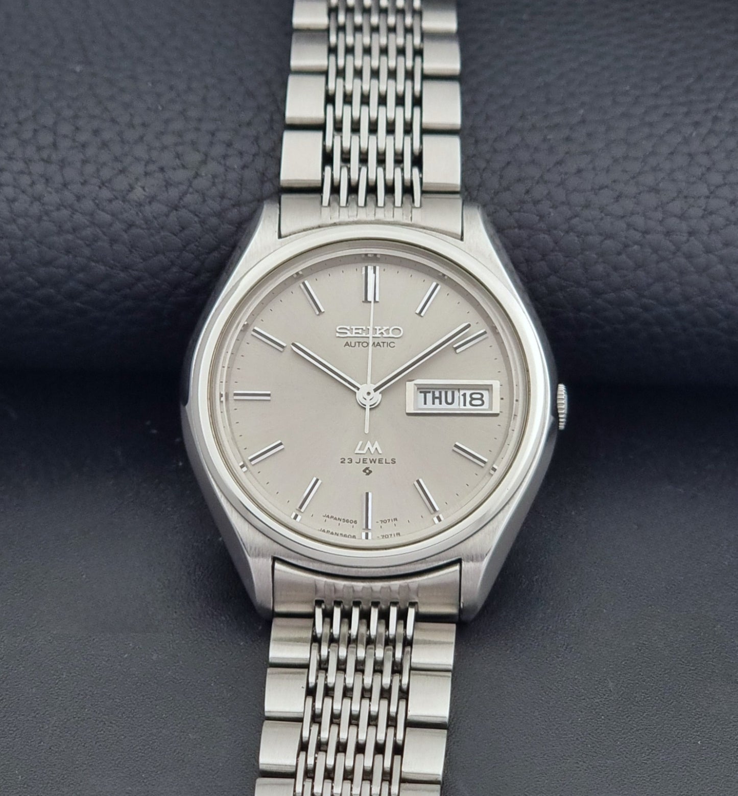 Vintage Seiko 5606-7071 LordMatic wristwatch with a metallic band on a dark gray background dial view