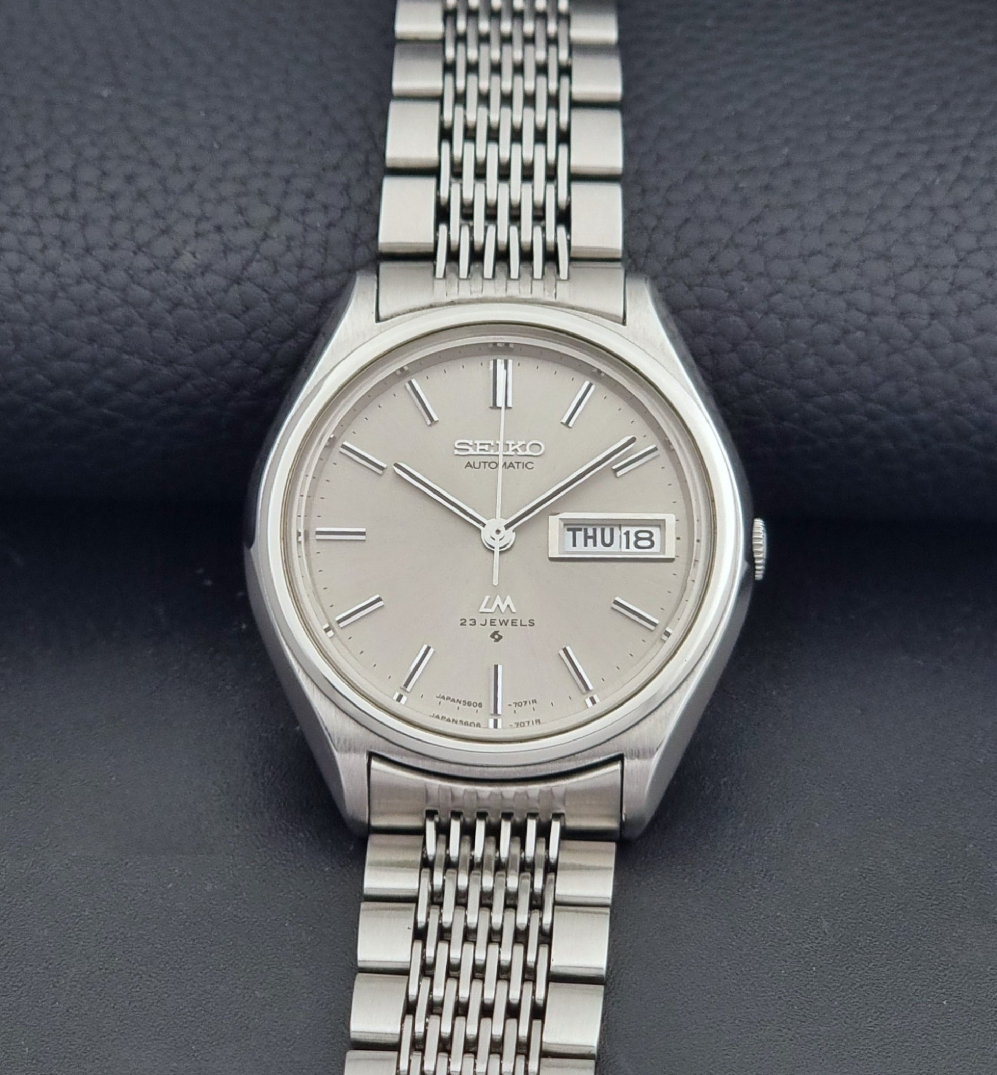 Vintage Seiko 5606-7071 LordMatic wristwatch with a metallic band on a dark gray background dial view