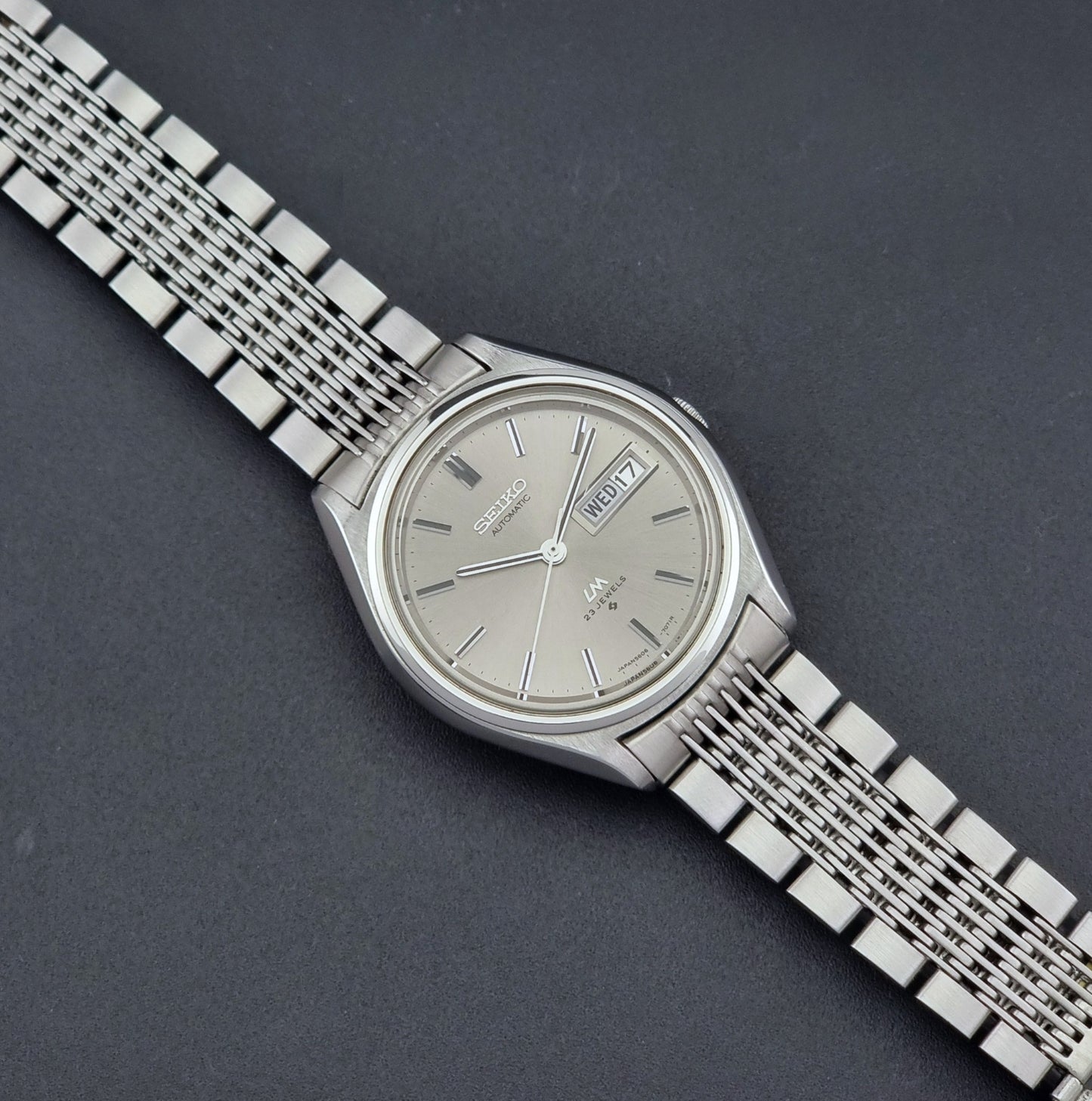 Vintage Seiko 5606-7071 LordMatic wristwatch with a metallic band on a dark gray background dial