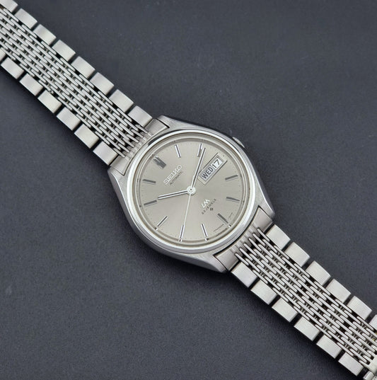 Vintage Seiko 5606-7071 LordMatic wristwatch with a metallic band on a dark gray background dial