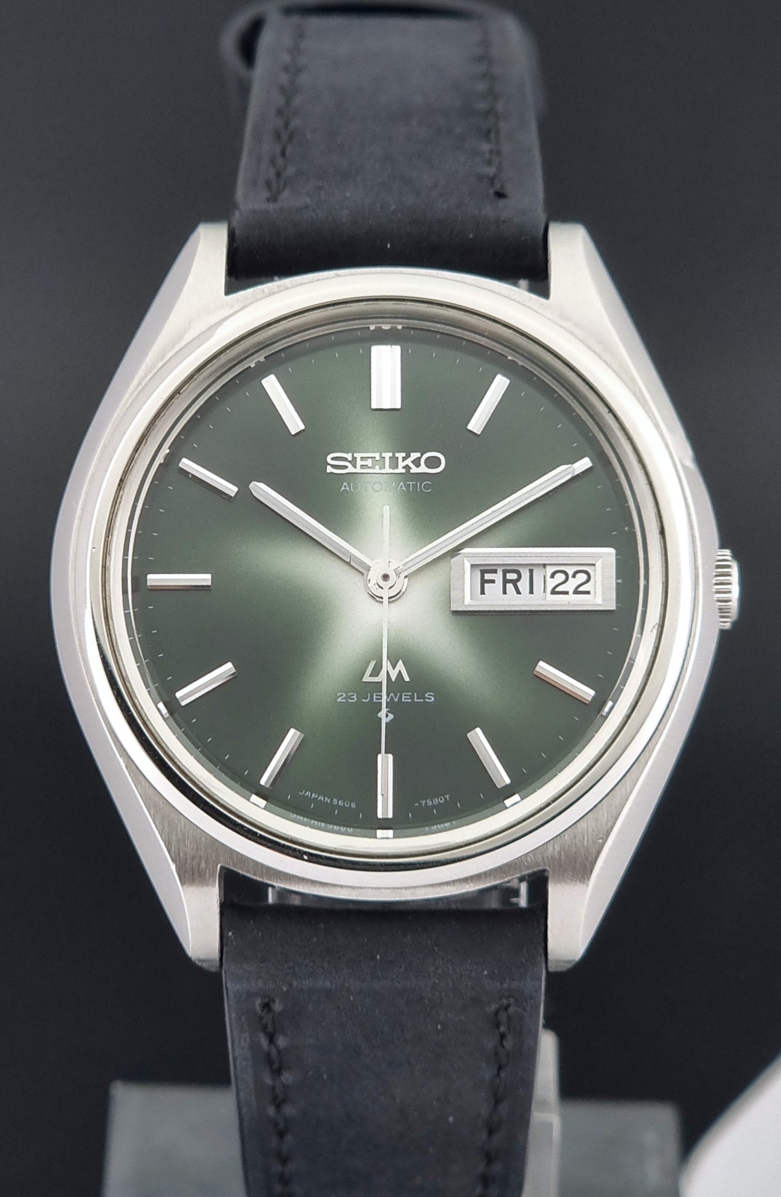 Front view of a Vintage Seiko Lord Matic watch with black leather strap and green dial on a dark background