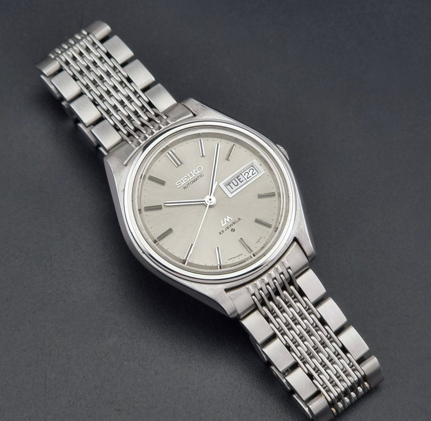 Vintage Seiko 5606-7071 watch LordMatic with a metallic band on a dark gray background close up dial view