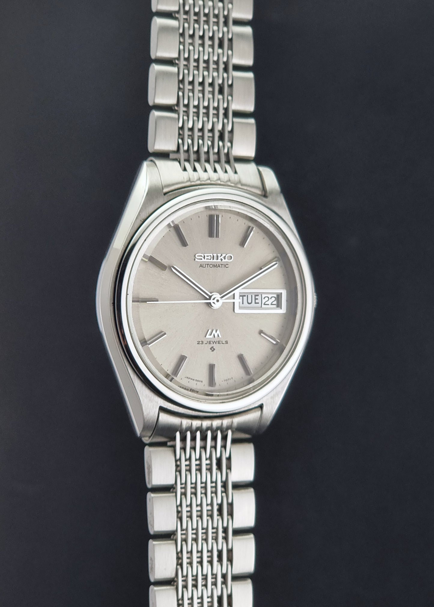 Vintage Seiko 5606-7071 watch LordMatic with a metallic band on a dark gray background side profile view
