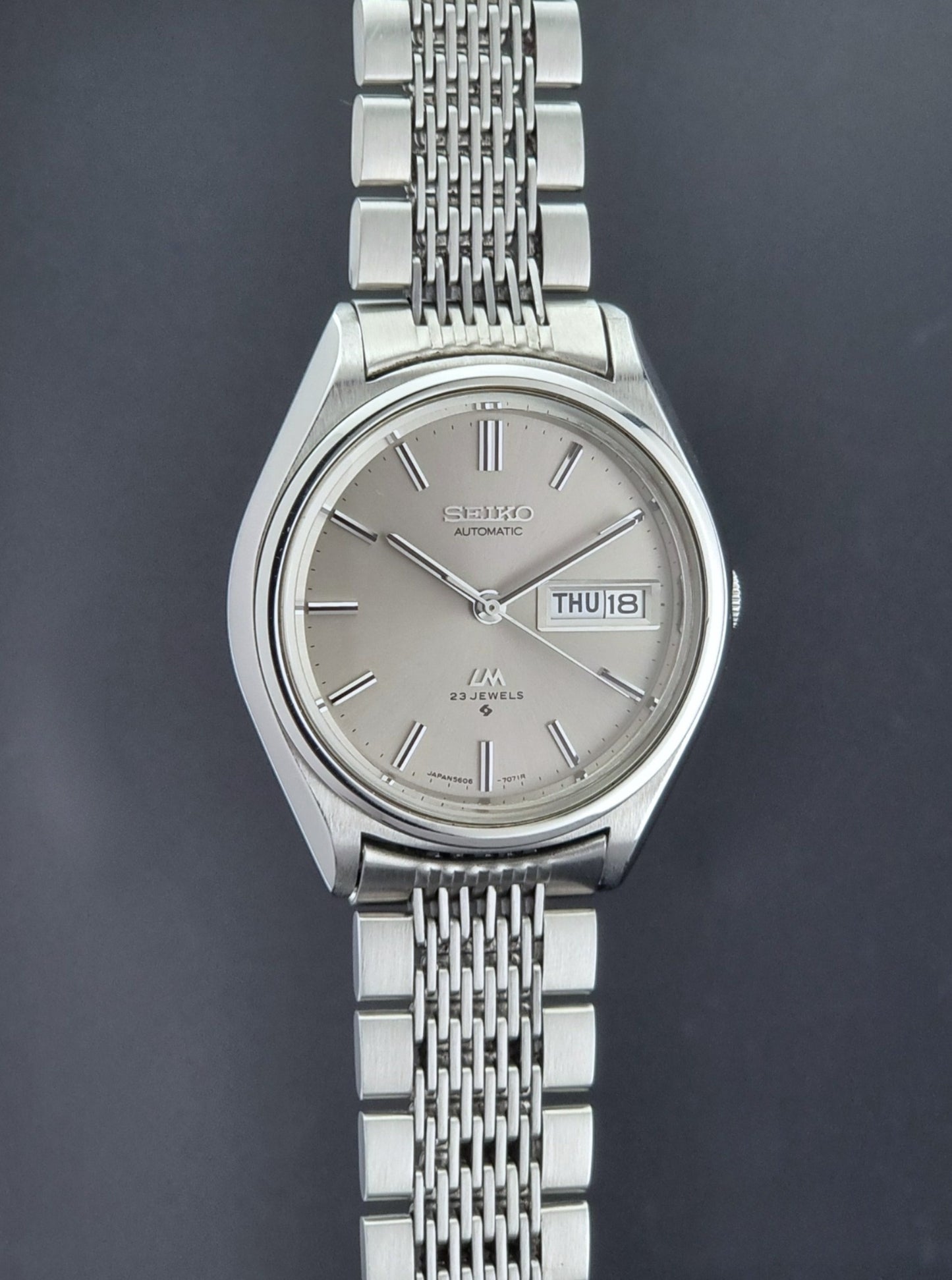 Vintage Seiko 5606-7071 LordMatic wristwatch with a metallic band on a dark gray background side profile view