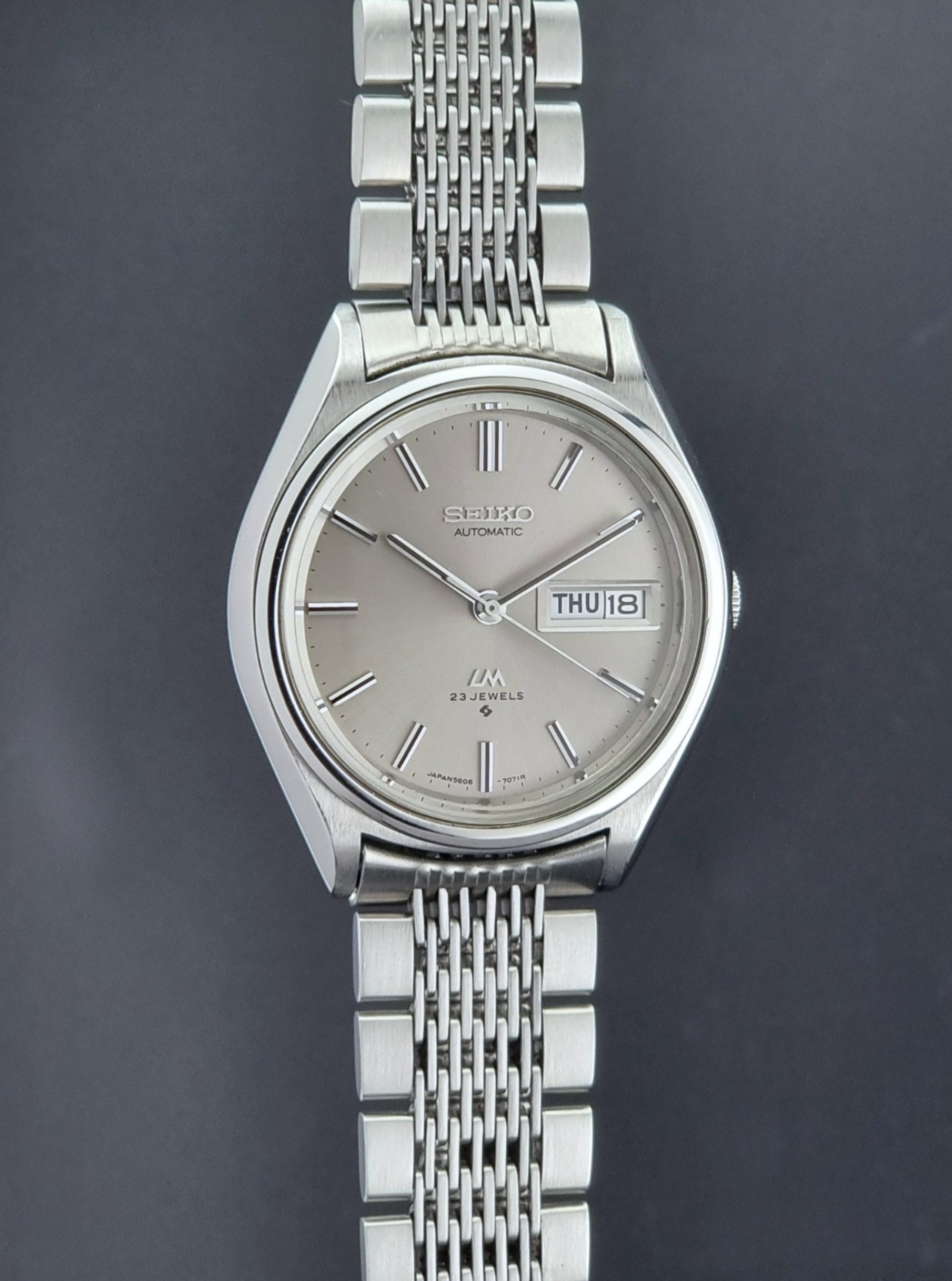 Vintage Seiko 5606-7071 LordMatic wristwatch with a metallic band on a dark gray background side profile view