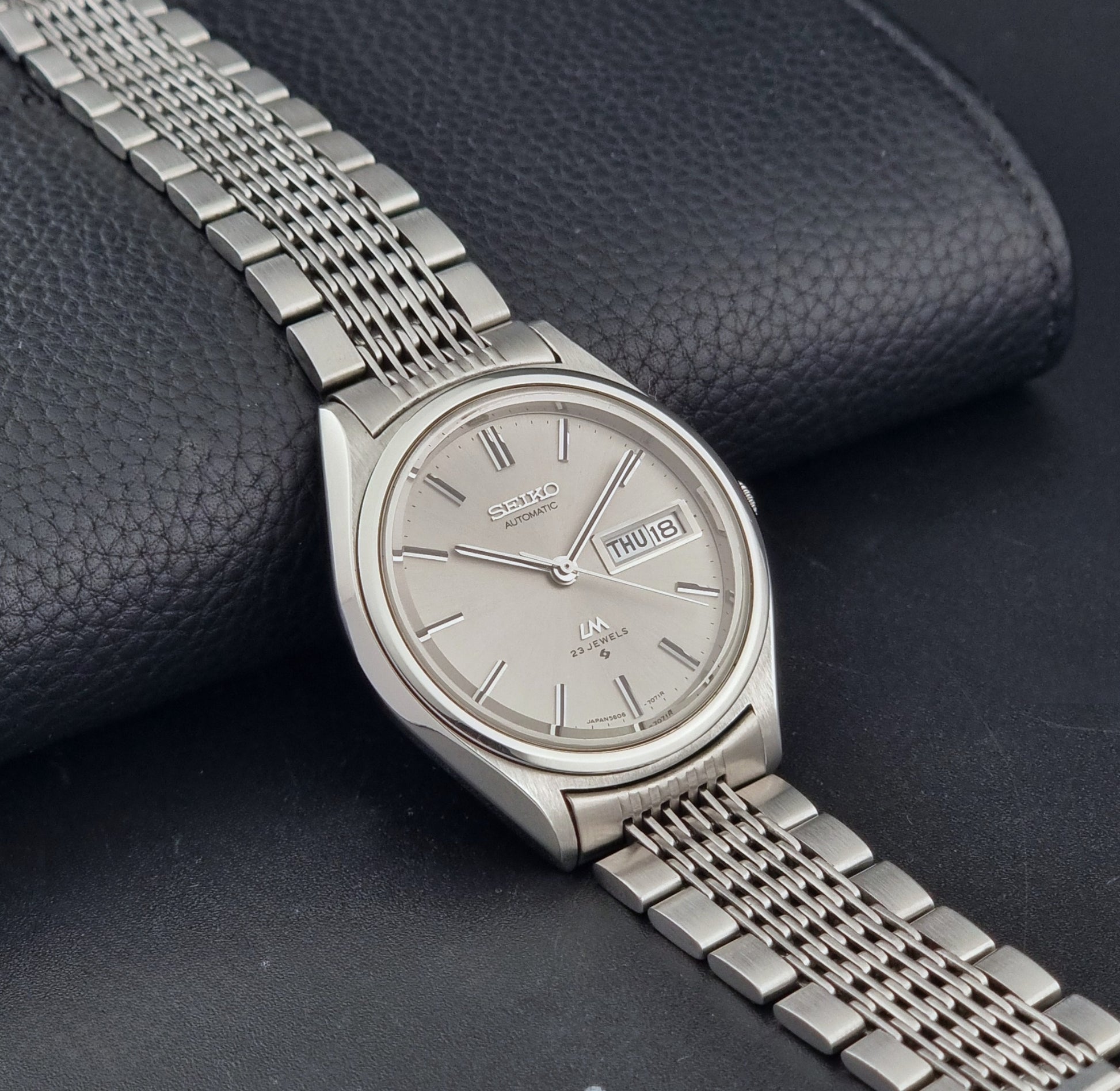 Vintage Seiko 5606-7071 LordMatic wristwatch with a metallic band on a dark gray background side view