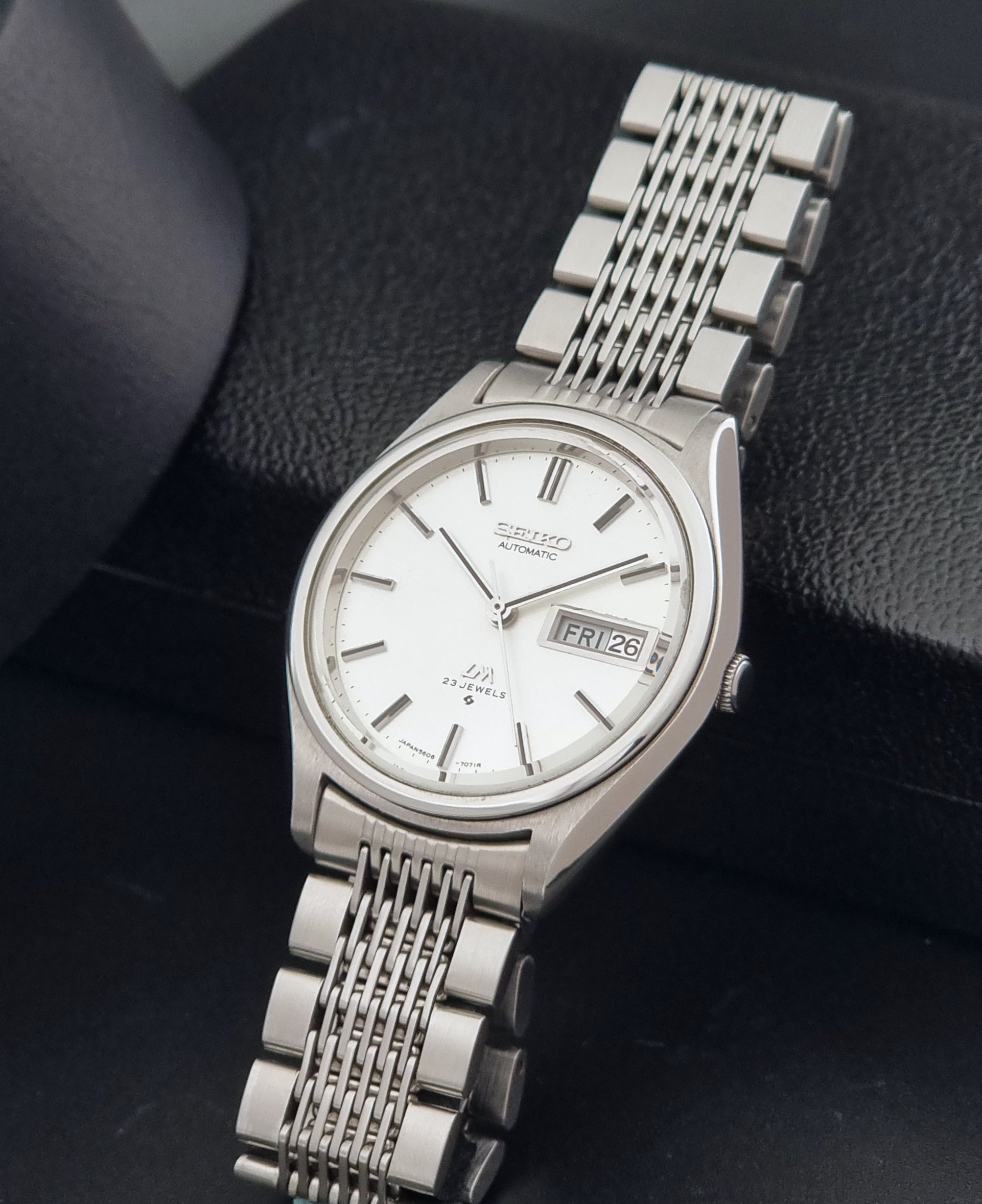 Vintage Seiko 5606-7071 watch LordMatic with a white dial and bracelet on a dark background crown view