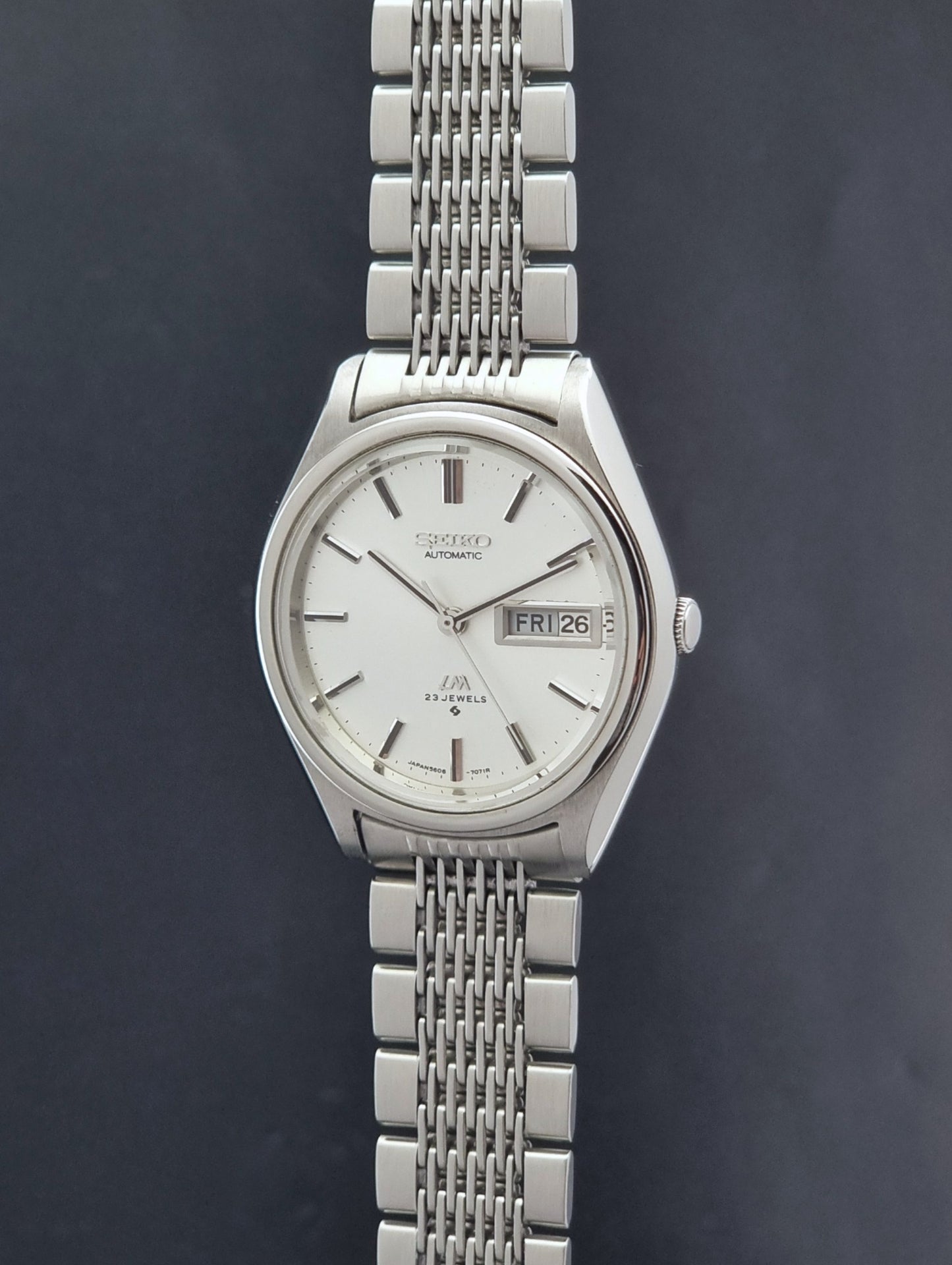 Vintage Seiko 5606-7071 watch LordMatic with a white dial and bracelet on a dark background crown profile view