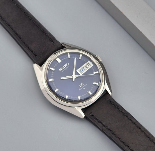 Vintage Seiko Wristwatch LordMatic 5606-7090 with a dark blue face and black leather strap on a grey background front