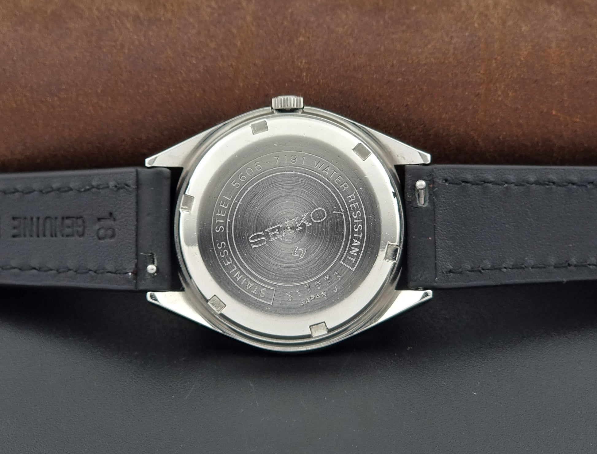 Vintage Seiko Wristwatch LordMatic 5606-7091 with a green face with black leather strap on a dark background case back view