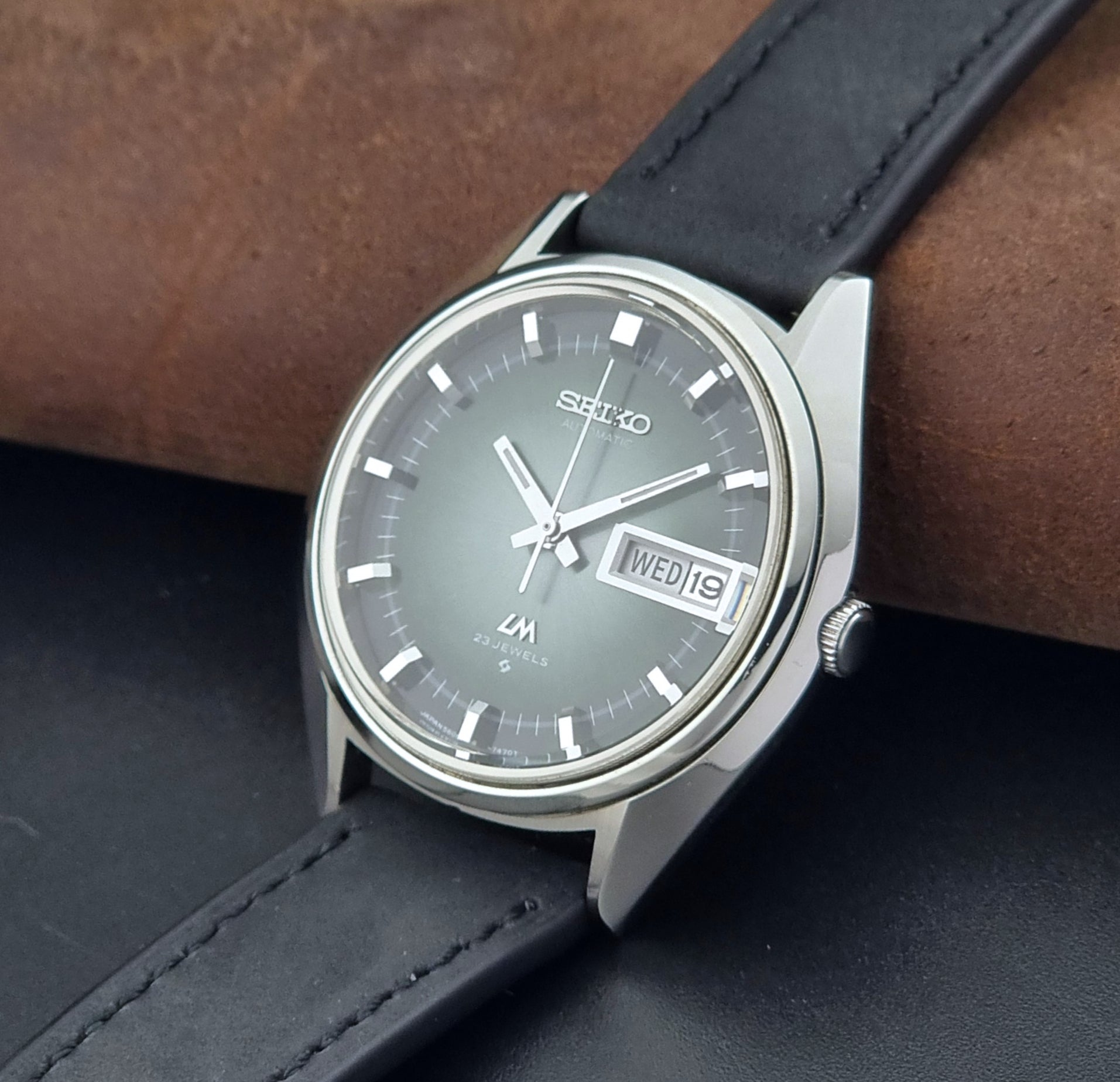 Vintage Seiko Wristwatch LordMatic 5606-7091 with a green face with black leather strap on a dark background crown view