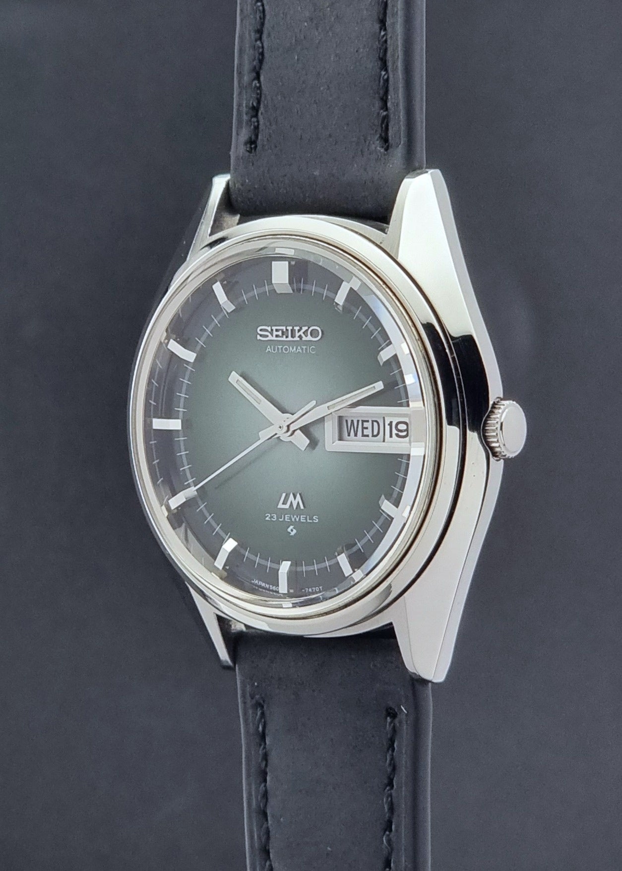 Vintage Seiko Wristwatch LordMatic 5606-7091 with a green face with black leather strap on a dark background crown profile view