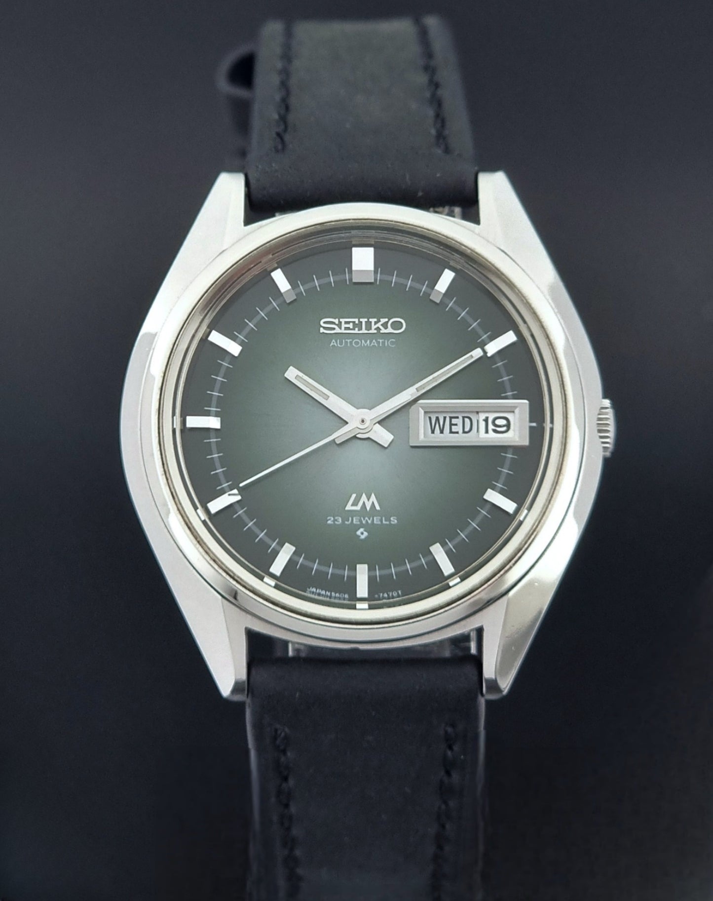 Vintage Seiko Wristwatch LordMatic 5606-7091 with a green face with black leather strap on a dark background close front view
