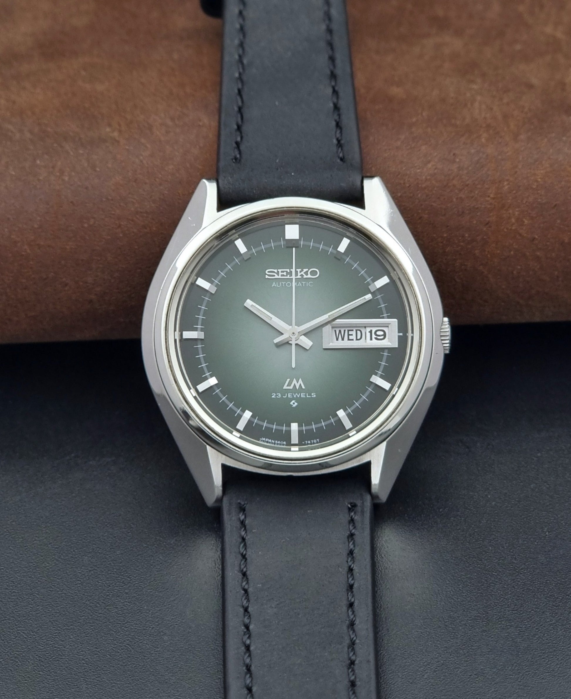 Vintage Seiko Wristwatch LordMatic 5606-7091 with a green face with black leather strap on a dark background front view