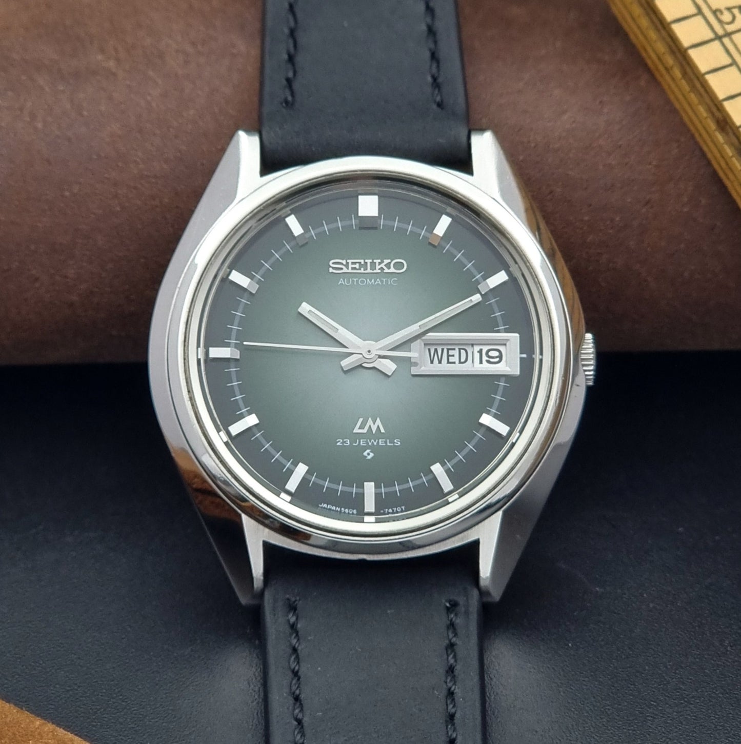 Vintage Seiko Wristwatch LordMatic 5606-7091 with a green face with black leather strap on a dark background close dial view