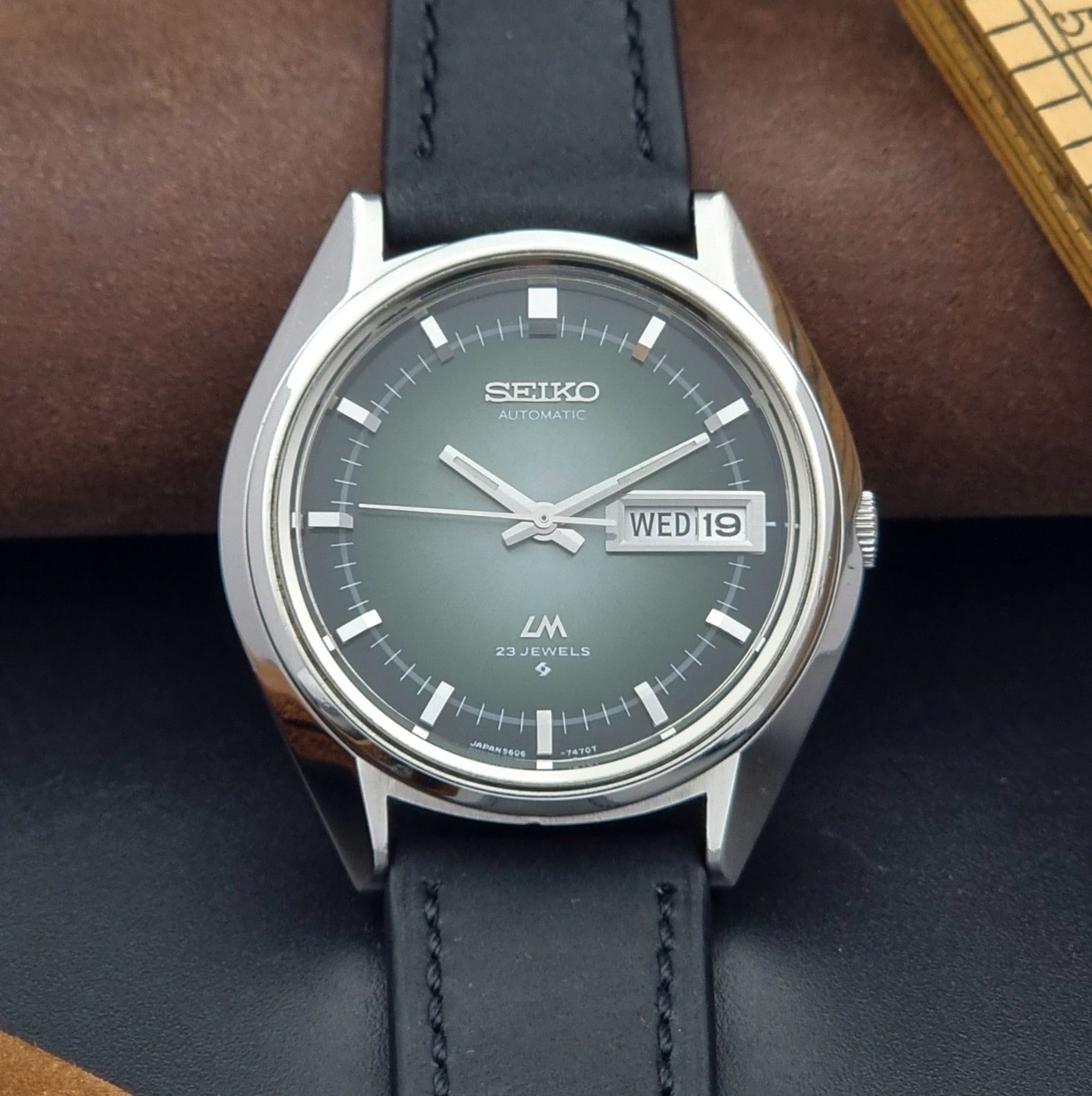 Vintage Seiko Wristwatch LordMatic 5606-7091 with a green face with black leather strap on a dark background close dial view