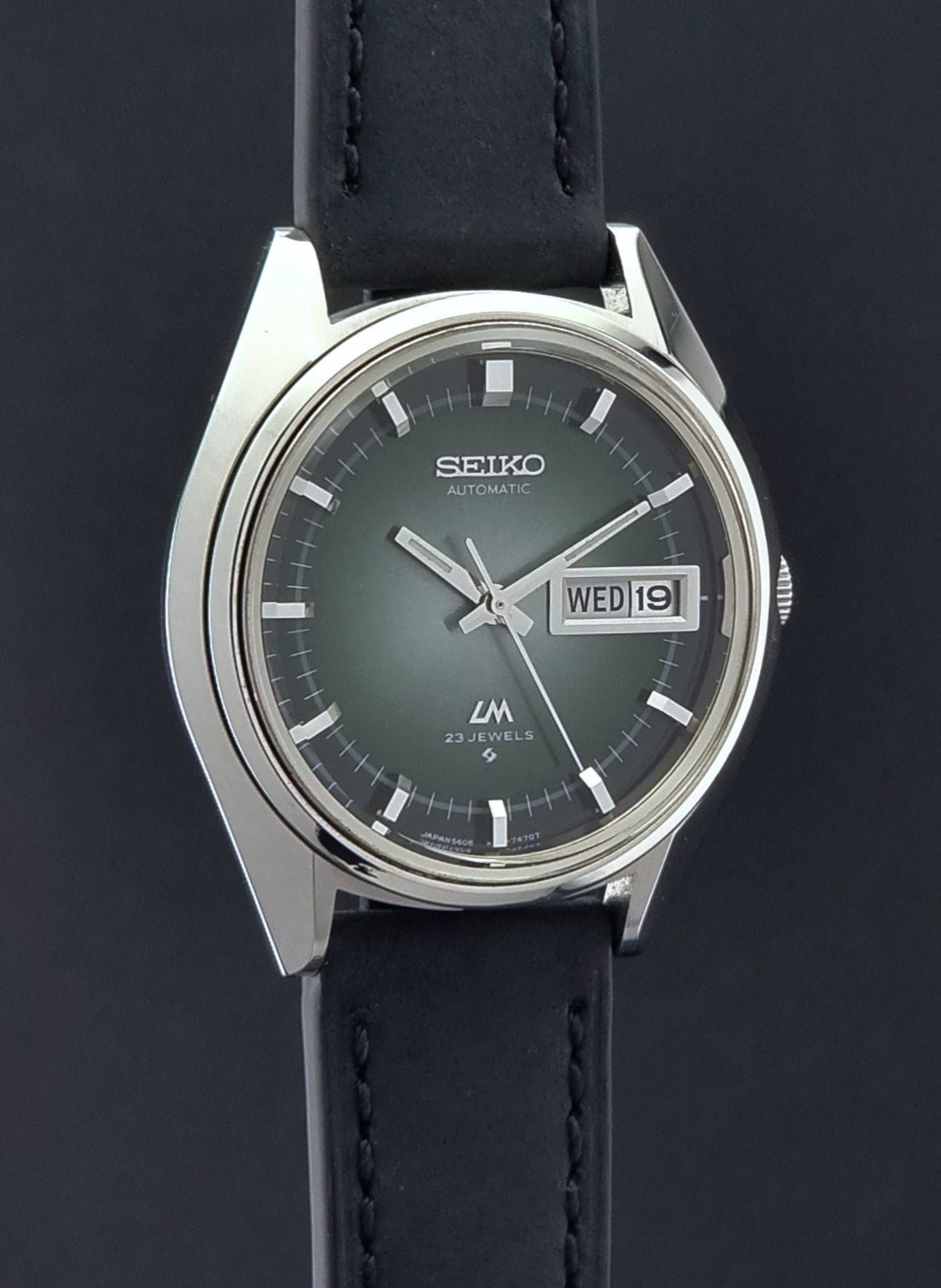 Vintage Seiko Wristwatch LordMatic 5606-7091 with a green face with black leather strap on a dark background side profile view