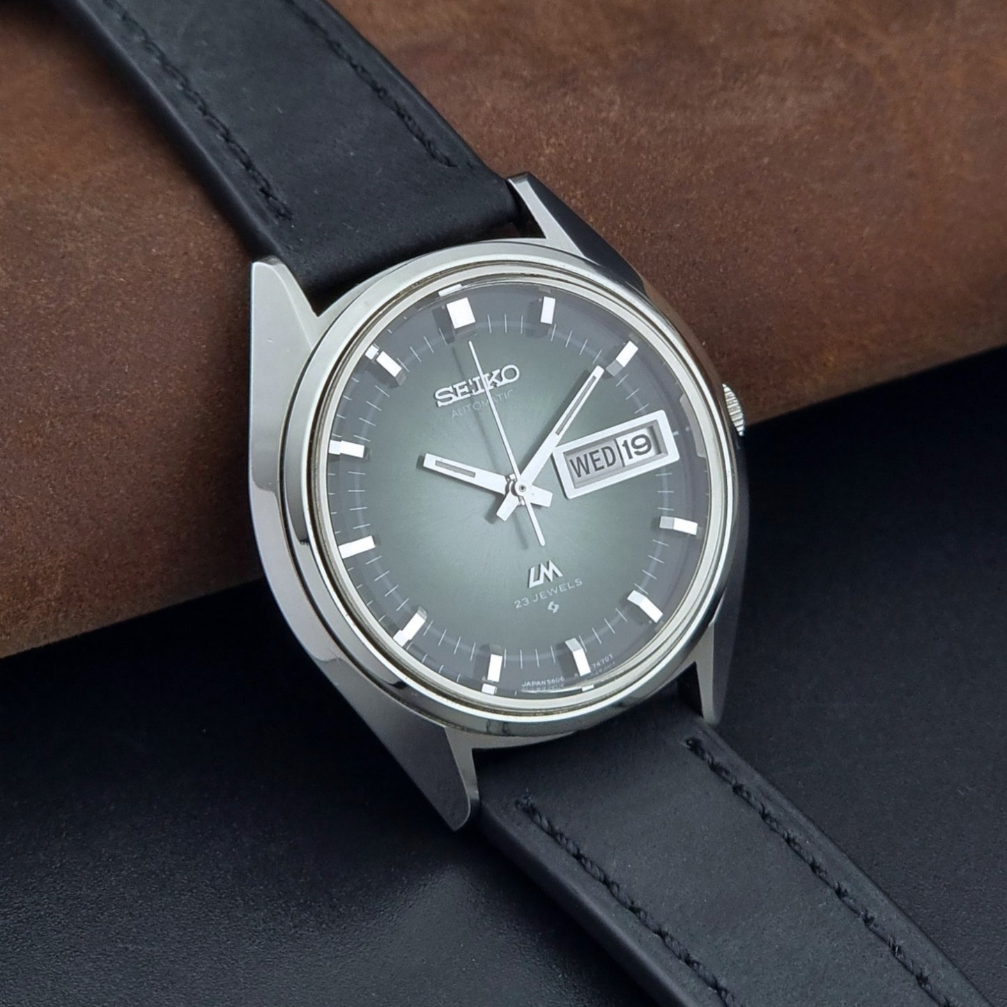 Vintage Seiko Wristwatch LordMatic 5606-7091 with a green face with black leather strap on a dark background side view