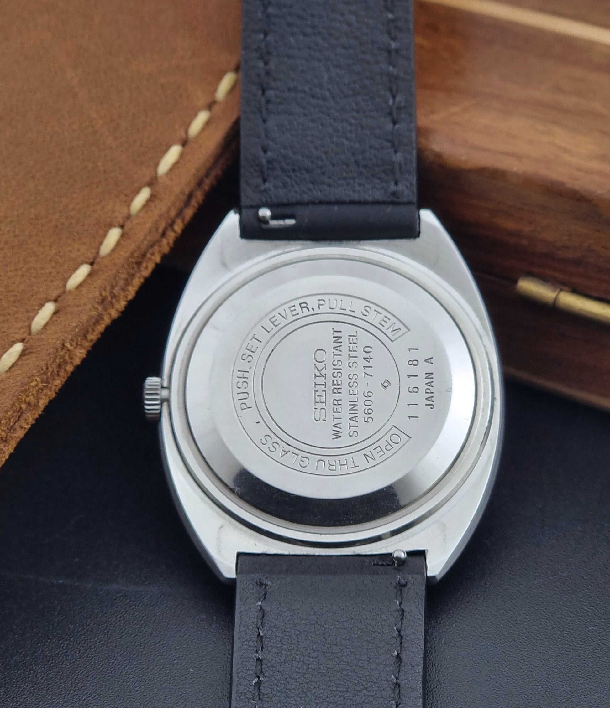 Vintage Seiko Lord Matic 5606-7150 Watch with black strap and gray dial on a wooden surface case back view