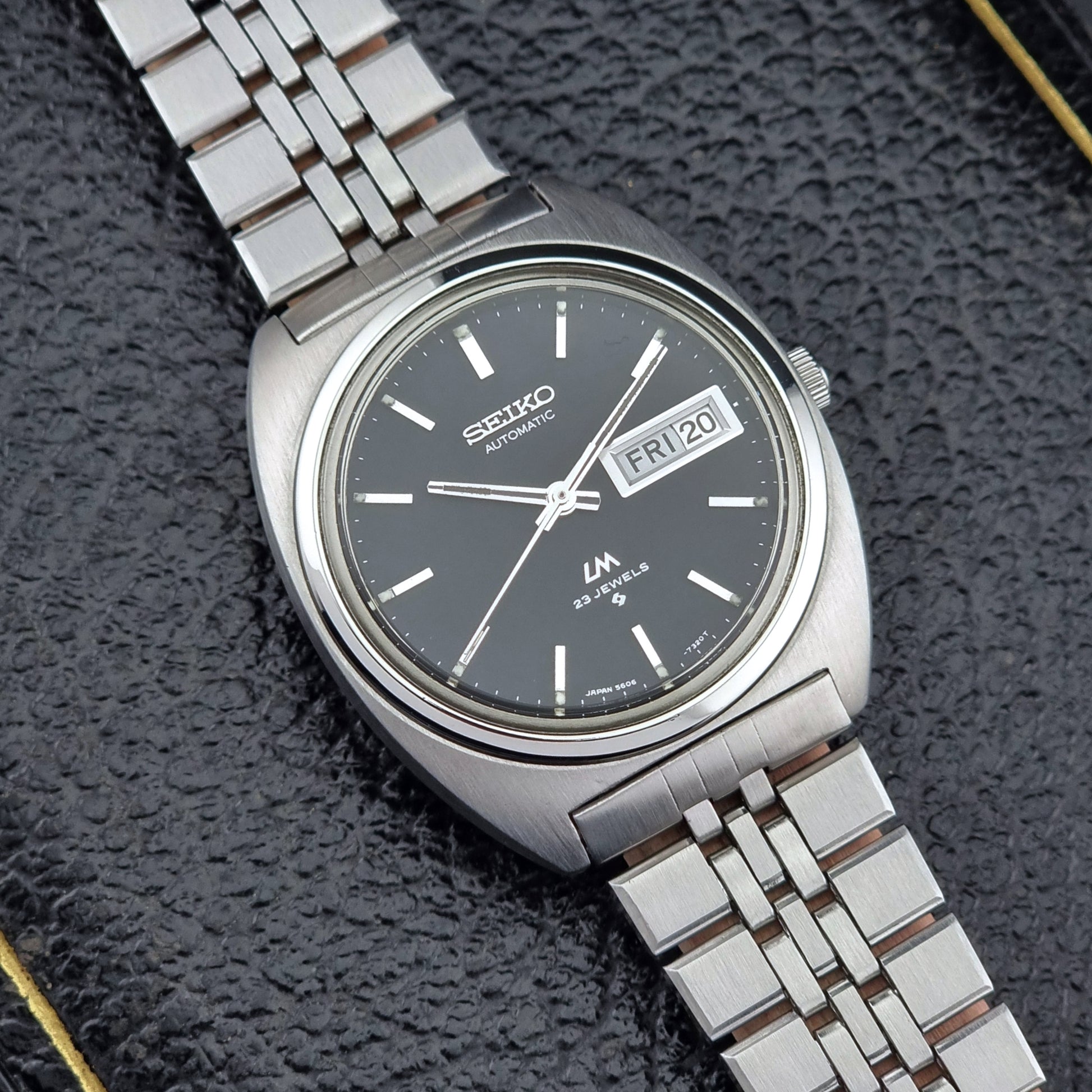 Vintage Seiko Lordmatic 5606-7140 watch with a dark face on a textured black background