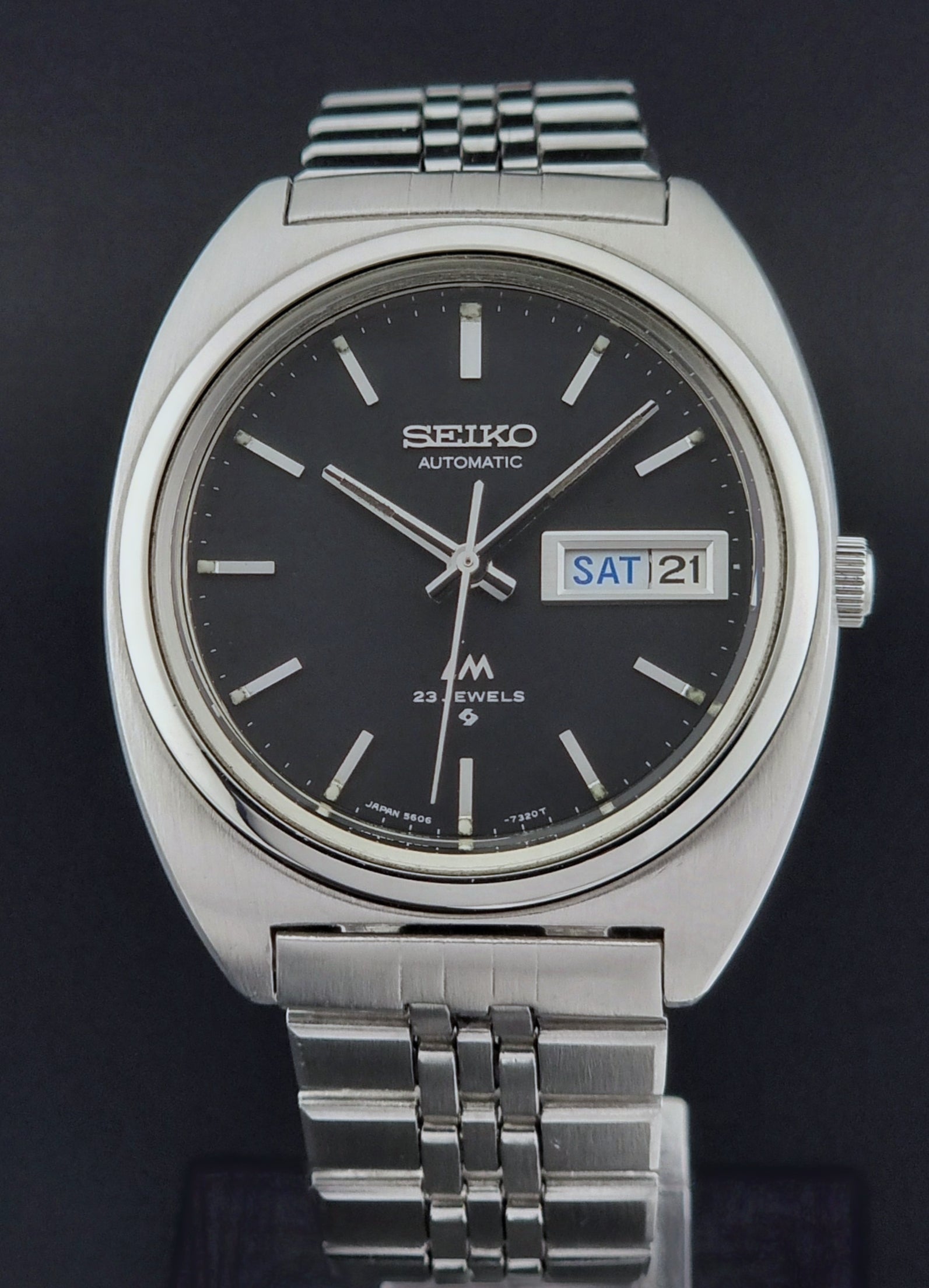 Vintage Seiko Lordmatic 5606-7140 watch with black dial and silver metal strap on a dark background