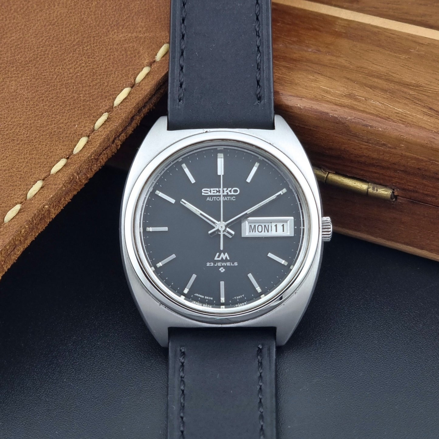Vintage Seiko Lord Matic 5606-7150 Watch with black strap and gray dial on a wooden surface front