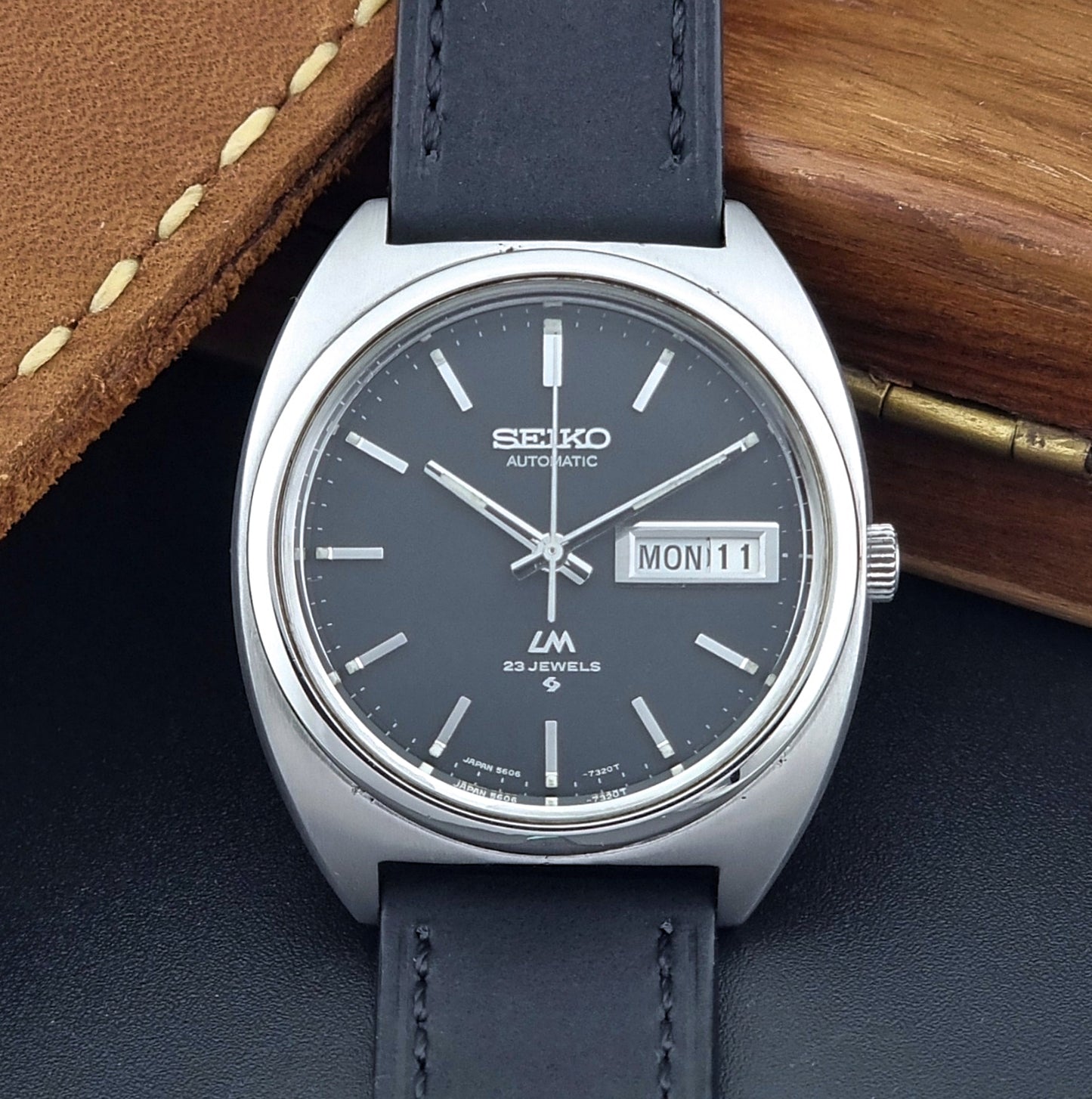 Vintage Seiko Lord Matic 5606-7150 Watch with black strap and gray dial on a wooden surface close up dial