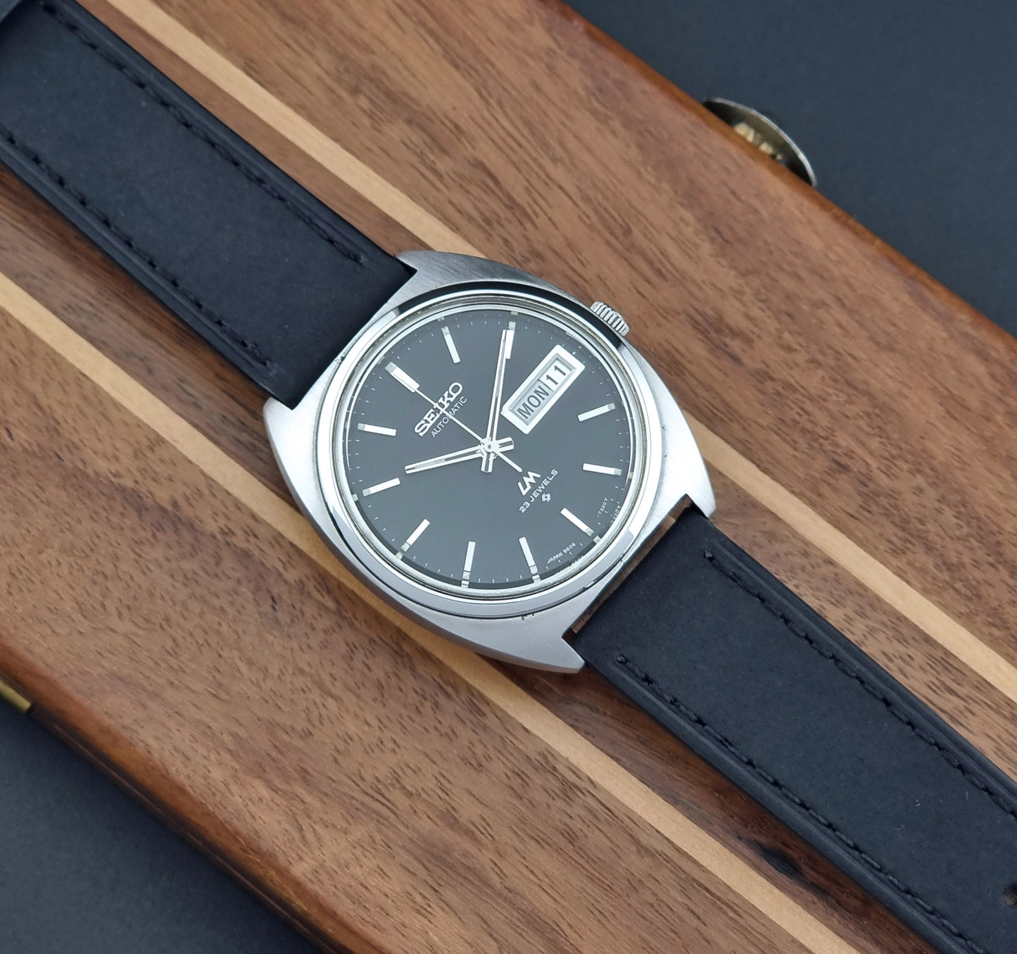 Vintage Seiko Lord Matic 5606-7150 Watch with black strap and gray dial on a wooden surface