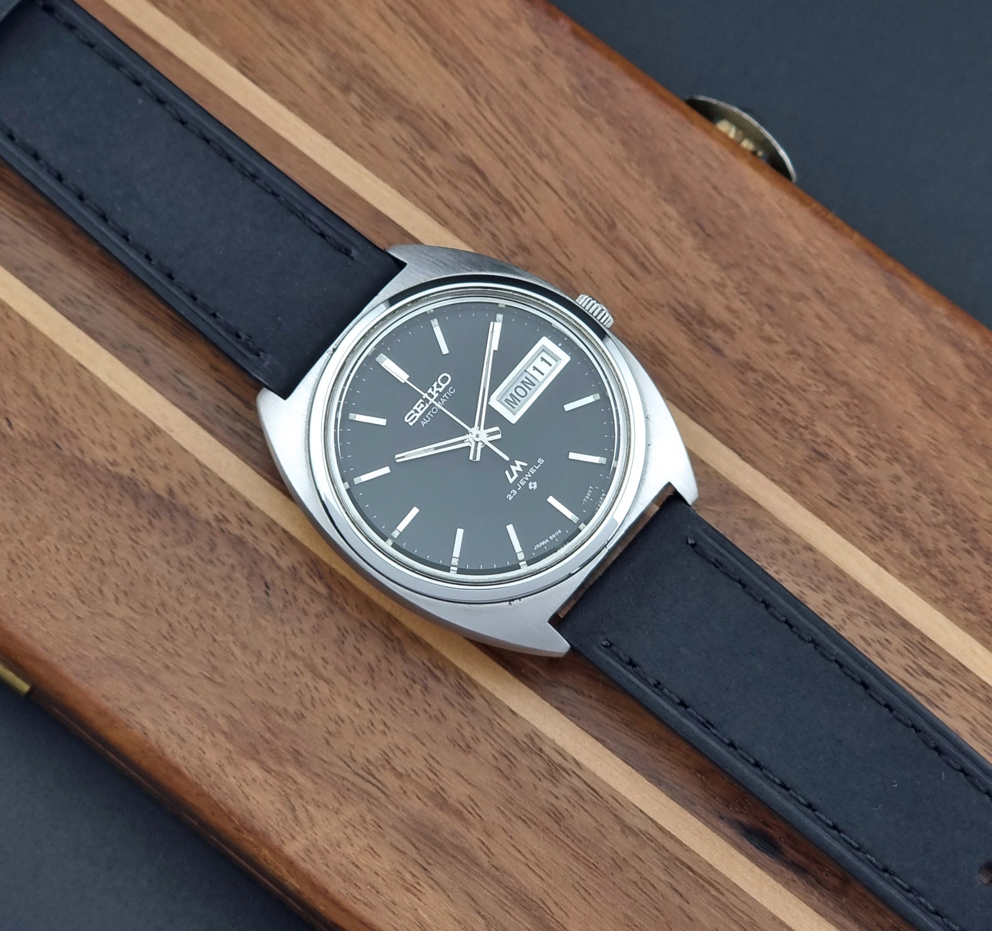 Vintage Seiko Lord Matic 5606-7150 Watch with black strap and gray dial on a wooden surface
