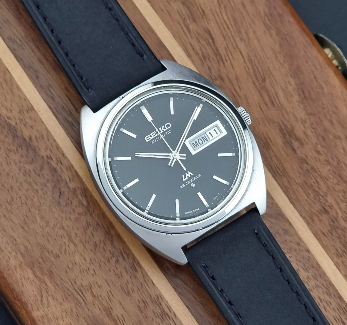 Vintage Seiko Lord Matic 5606-7150 Watch with black strap and gray dial on a wooden surface dial view