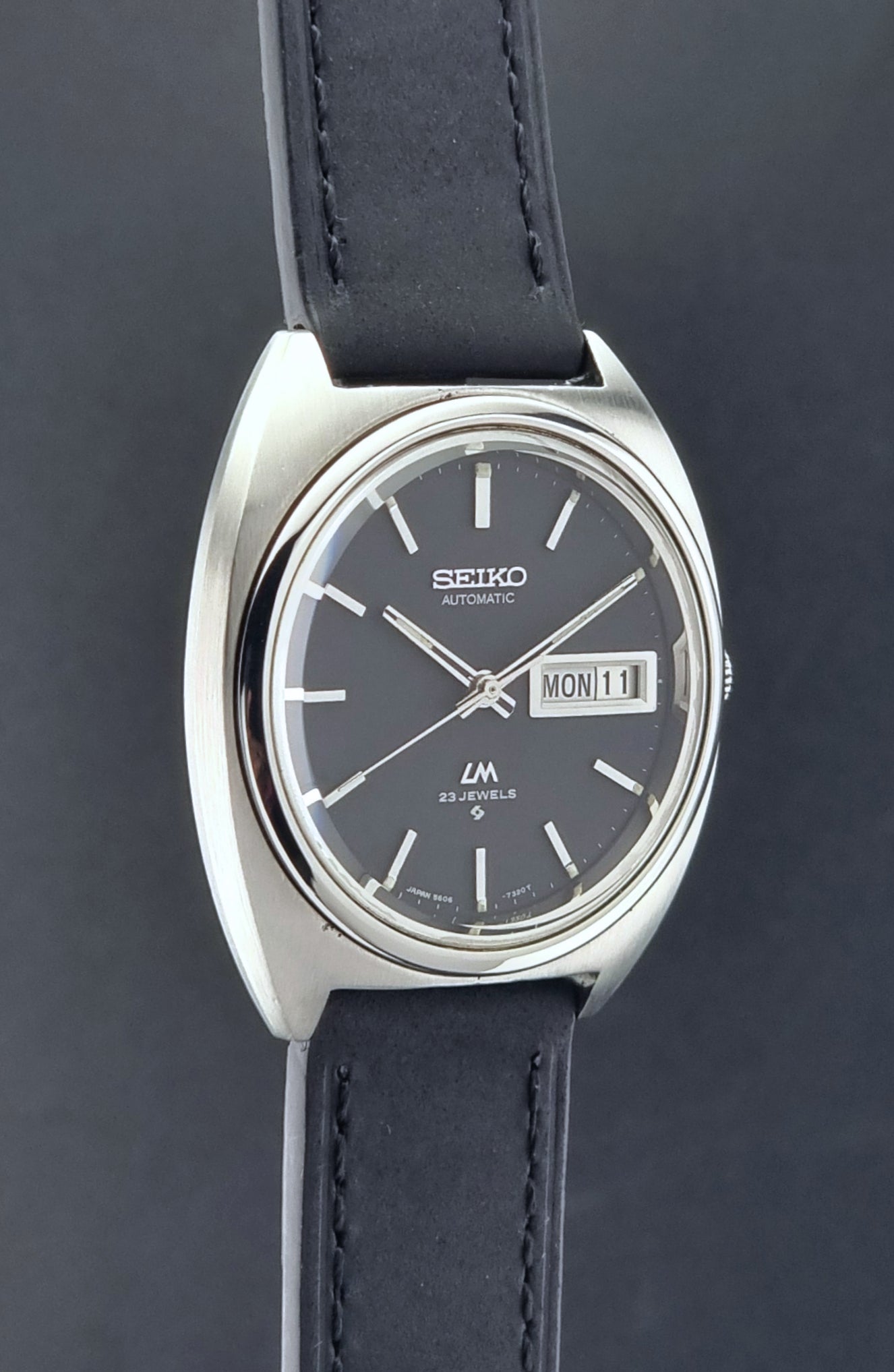 Vintage Seiko Lord Matic 5606-7150 Watch with black strap and gray dial on a wooden surface side profile