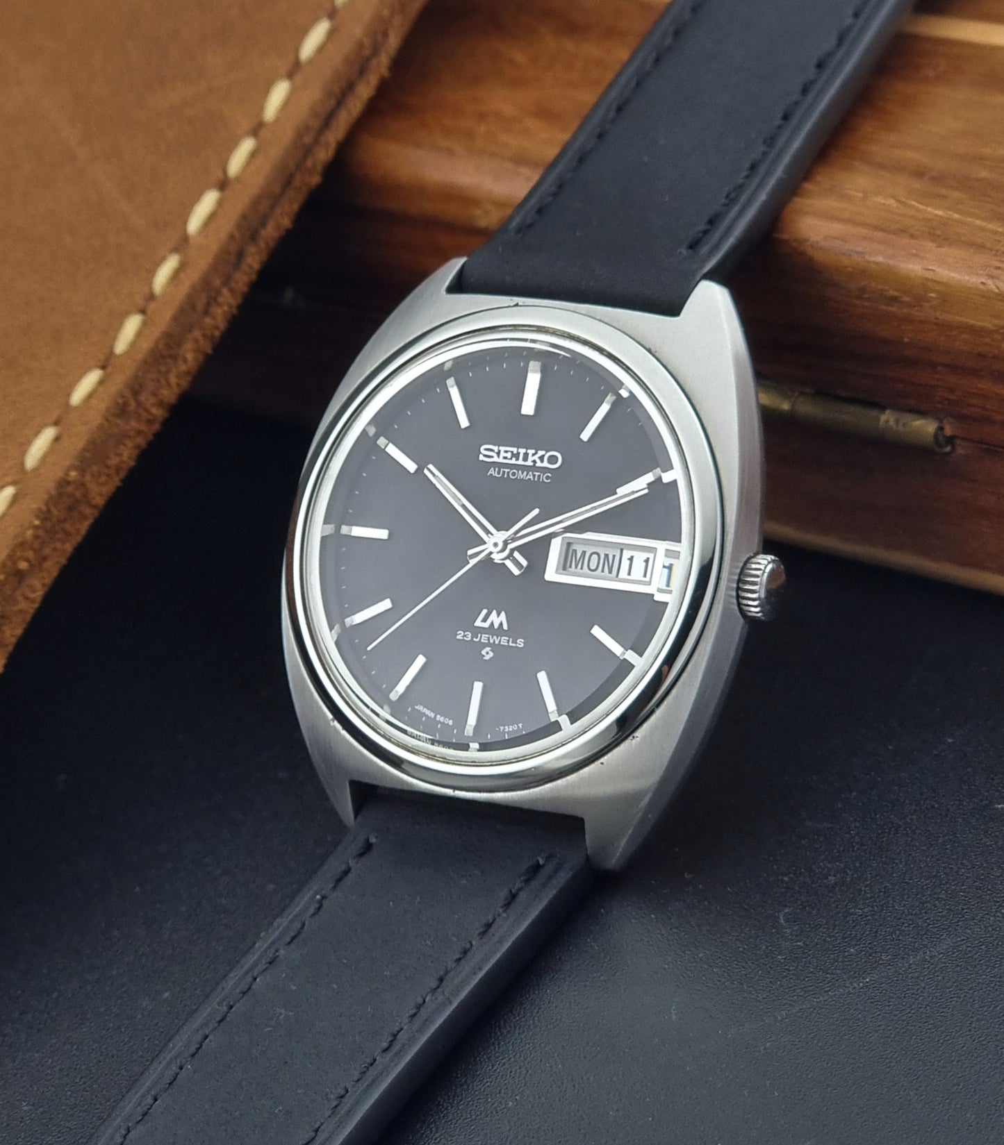 Vintage Seiko Lord Matic 5606-7150 Watch with black strap and gray dial on a wooden surface crown view