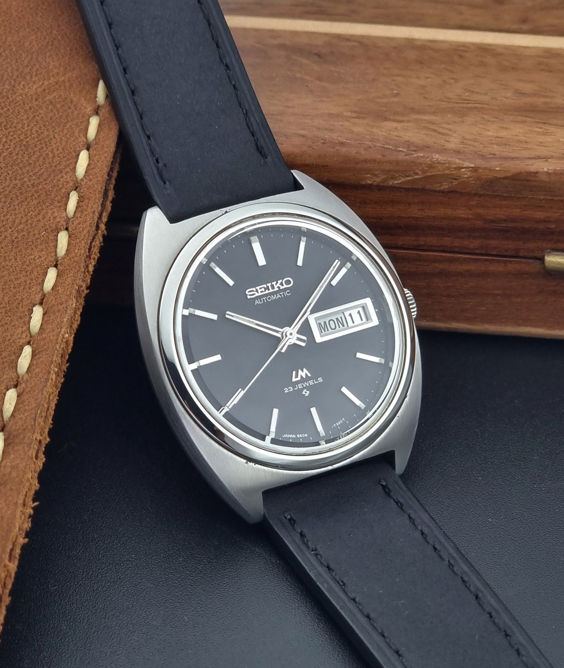 Vintage Seiko Lord Matic 5606-7150 Watch with black strap and gray dial on a wooden surface side view
