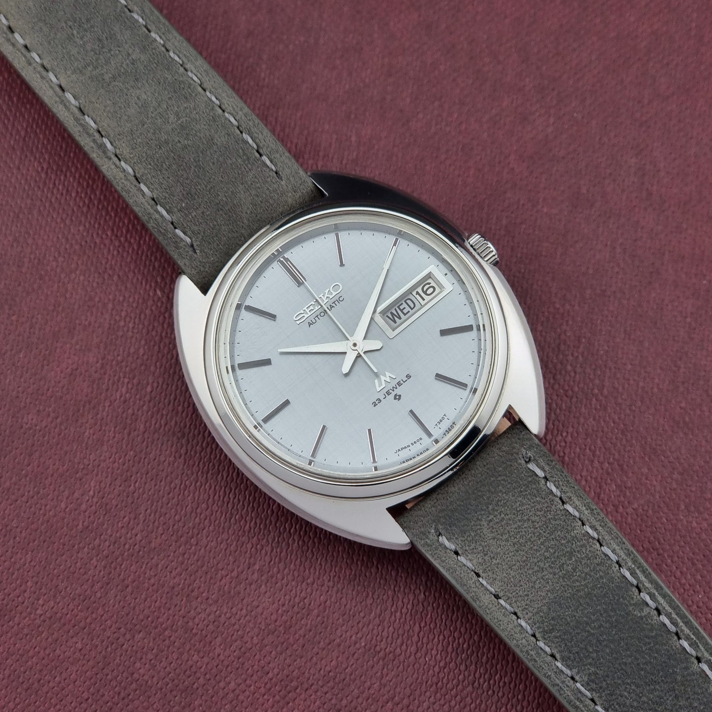 Seiko watch with gray strap on a maroon background