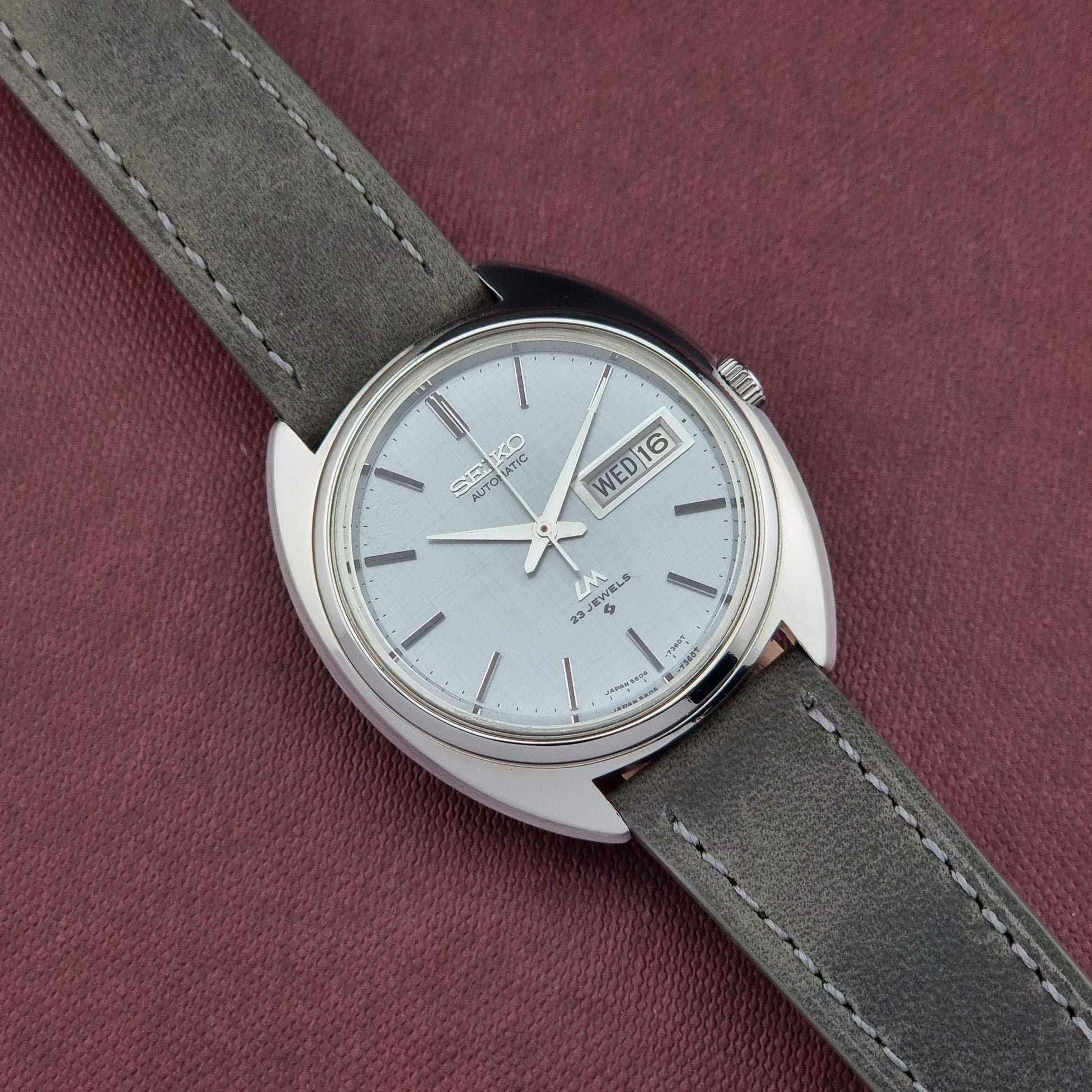 Seiko watch with gray strap on a maroon background