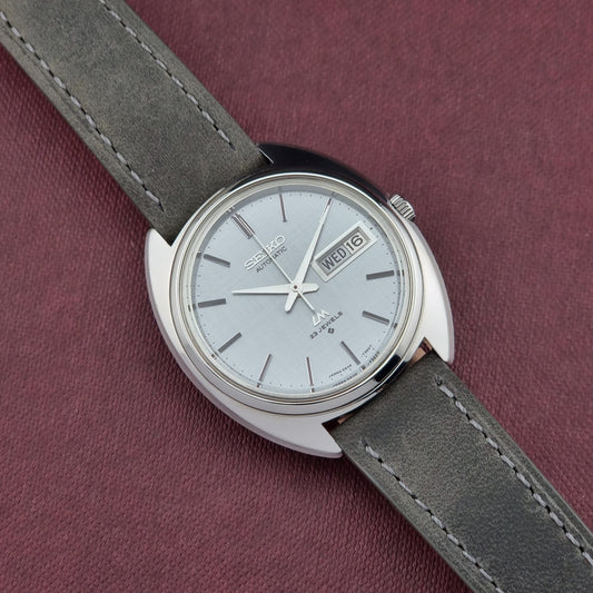 Seiko watch with gray strap on a maroon background