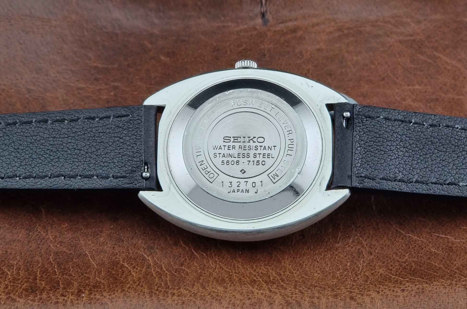 Vintage Seiko watch LordMatic 5606-7150 with black leather strap on a brown leather surface case back