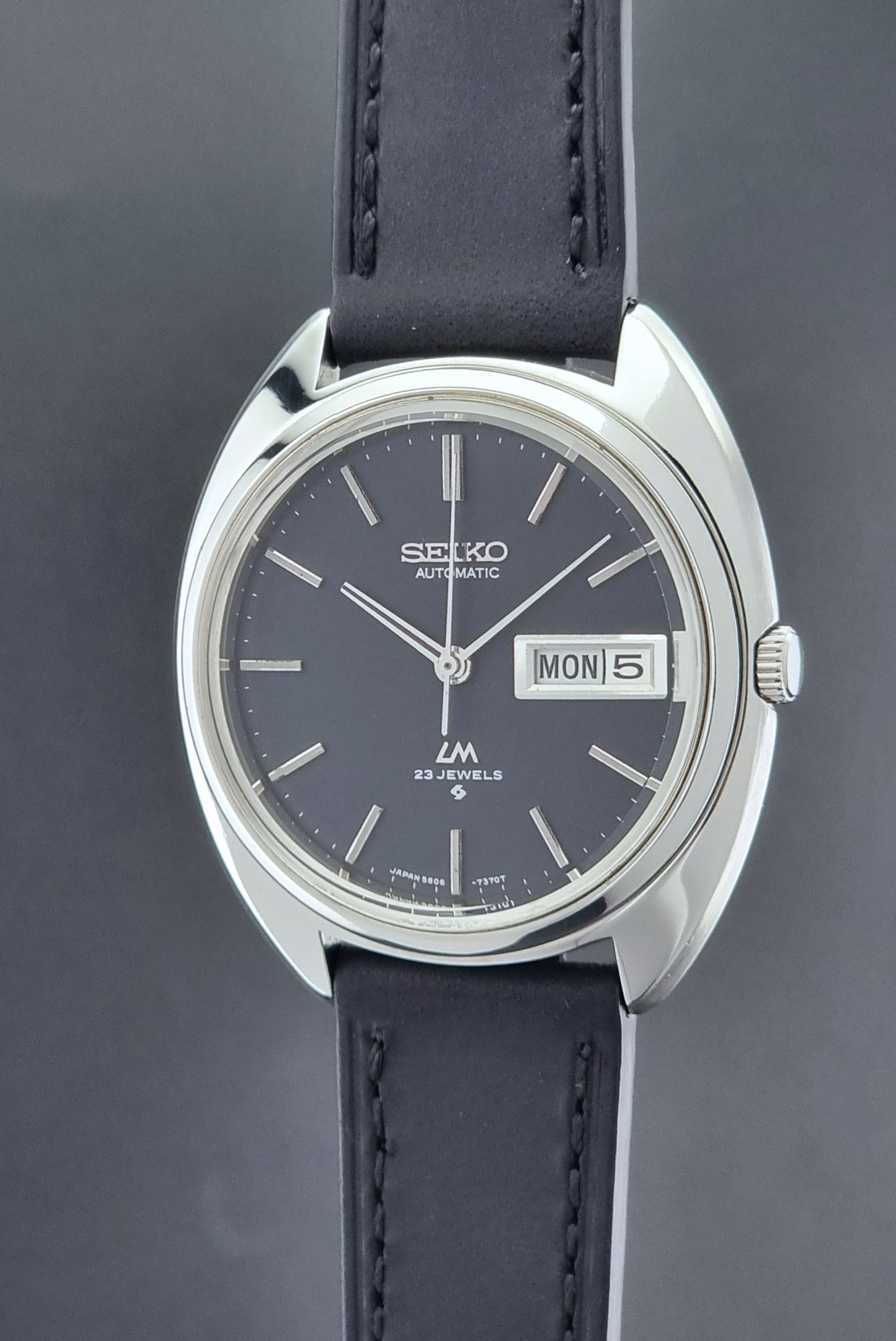 Vintage Seiko watch LordMatic 5606-7150 with black leather strap on a brown leather surface crown side profile