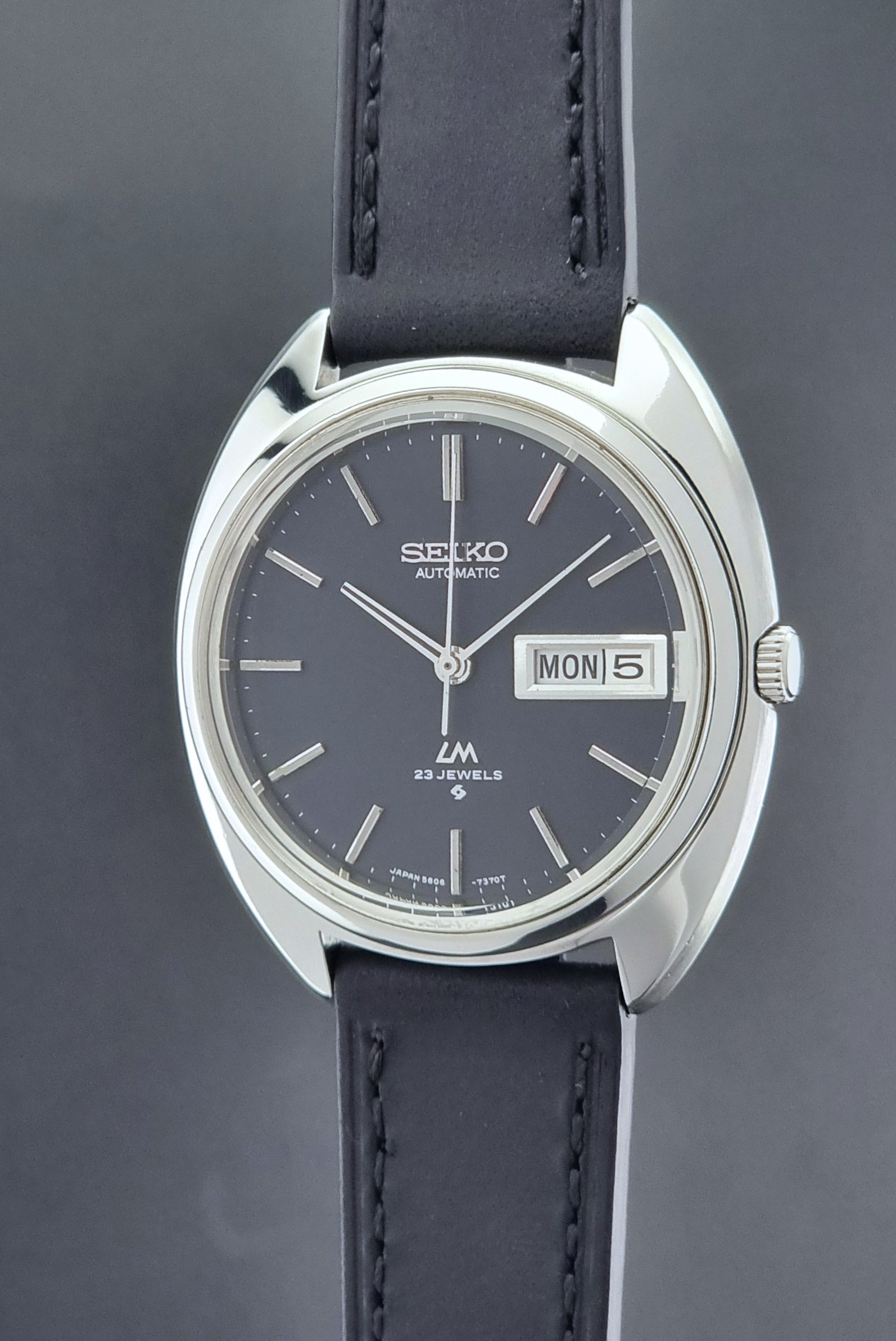 Vintage Seiko watch LordMatic 5606-7150 with black leather strap on a brown leather surface crown side profile