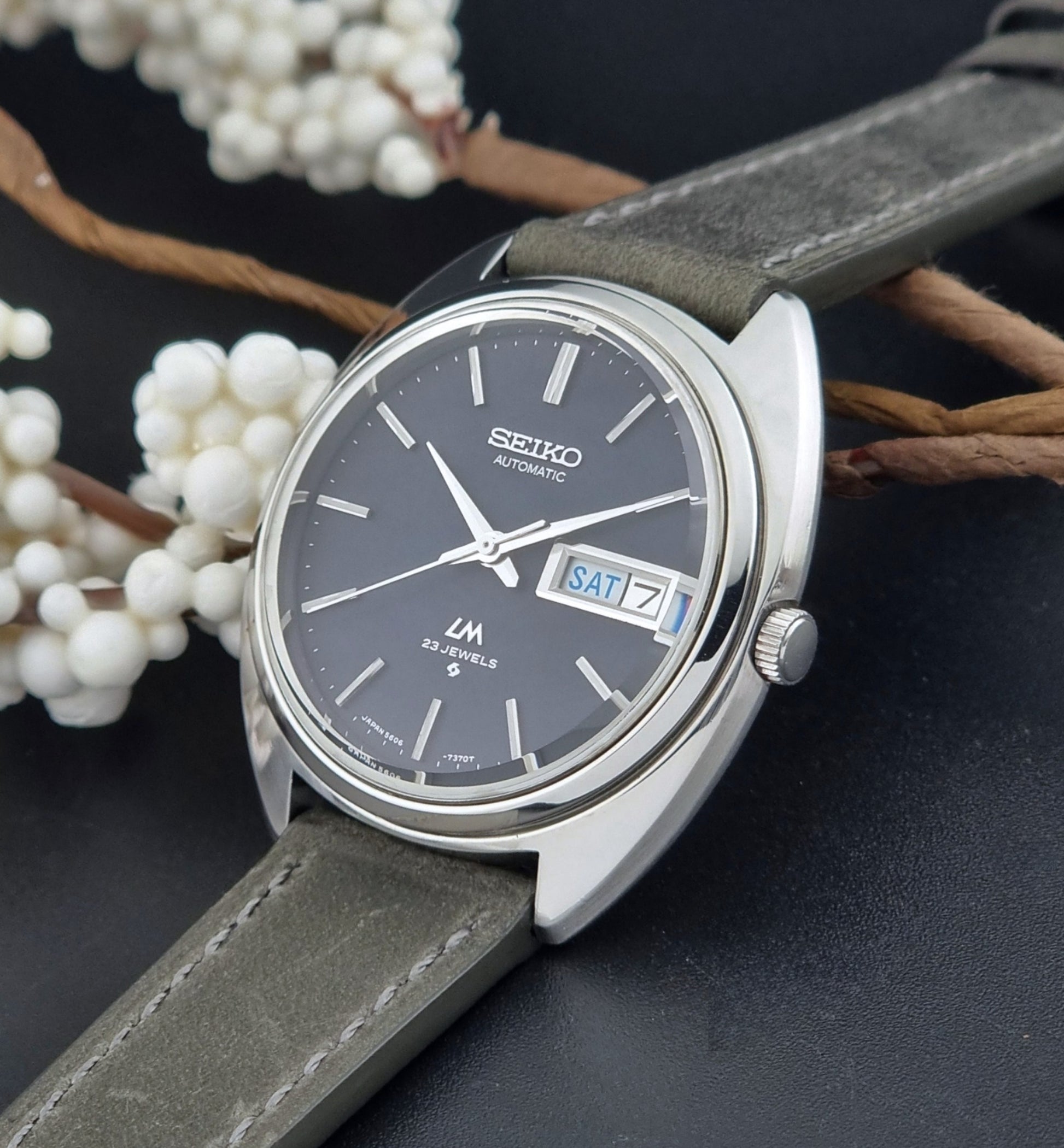 Vintage Seiko Lordmatic 5606-7150 wristwatch with a dark gray strap on a dark background crown view