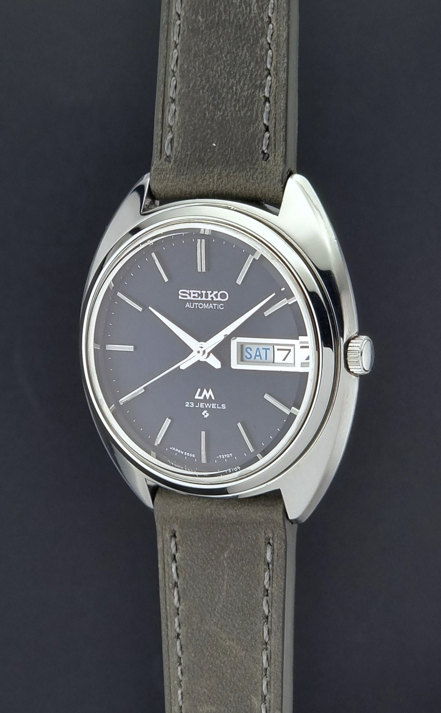 Vintage Seiko Lordmatic 5606-7150 wristwatch with a dark gray strap on a dark background crown profile view