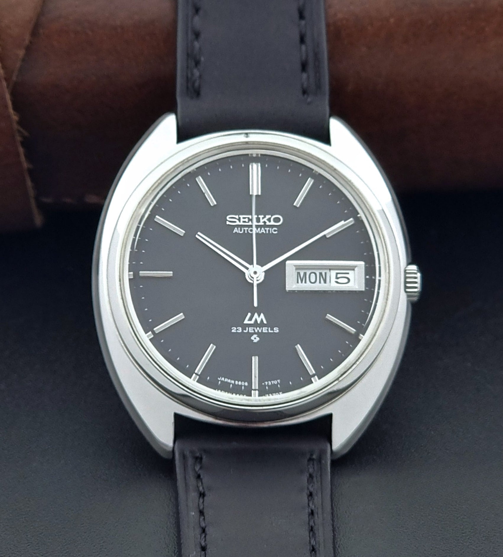 Vintage Seiko watch LordMatic 5606-7150 with black leather strap on a brown leather surface close up front