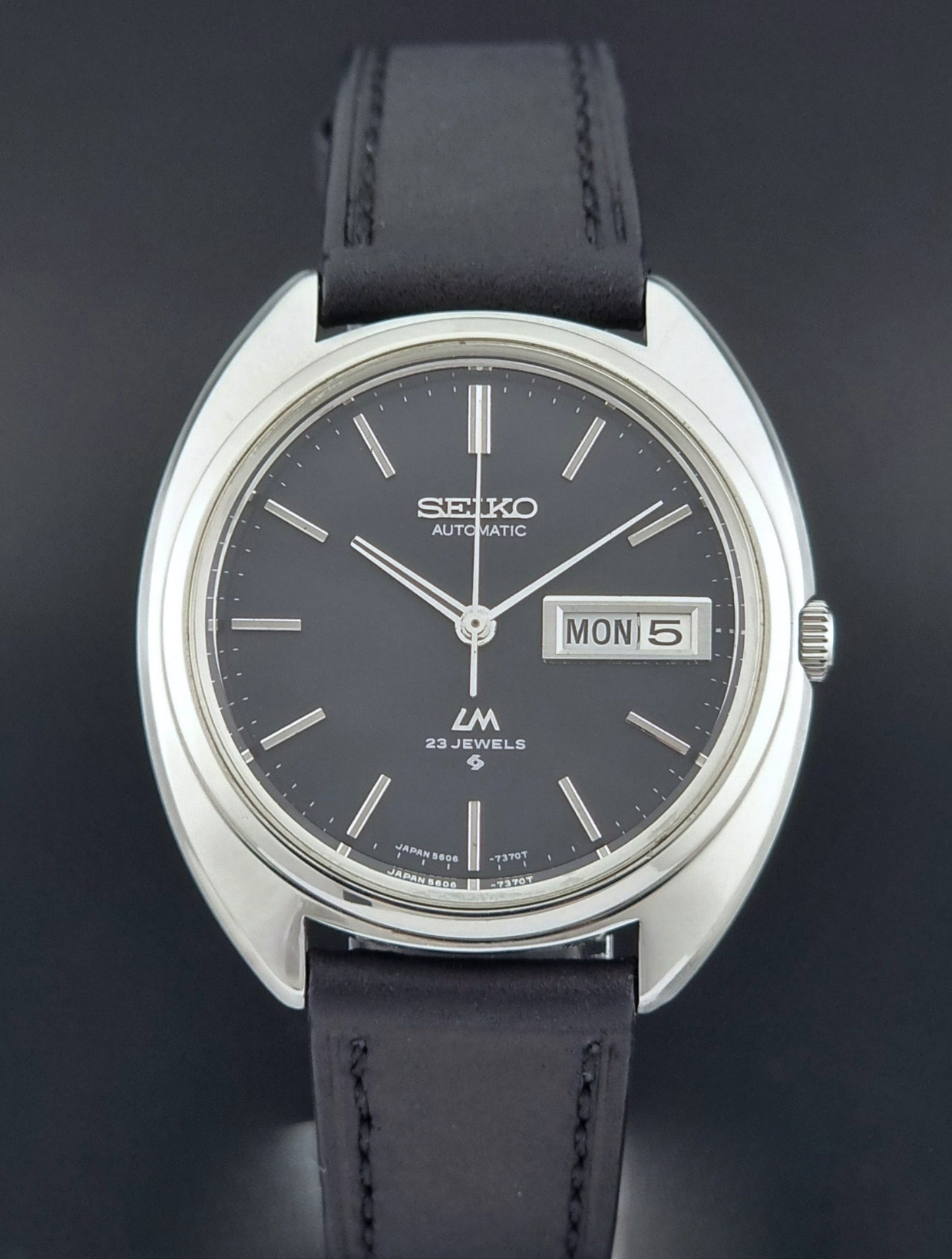 Vintage Seiko watch LordMatic 5606-7150 with black leather strap on a brown leather surface front view